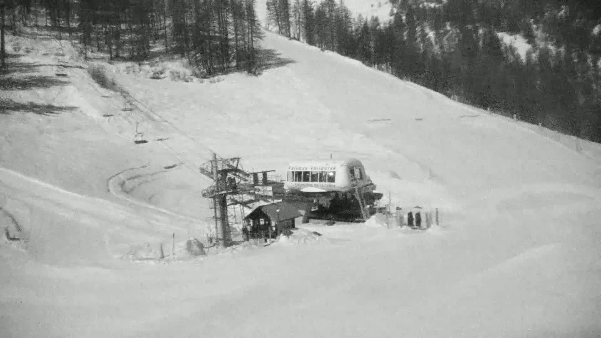 A snow-covered ski slope with a chairlift and a small building at the bottom, under a cloudy sky.