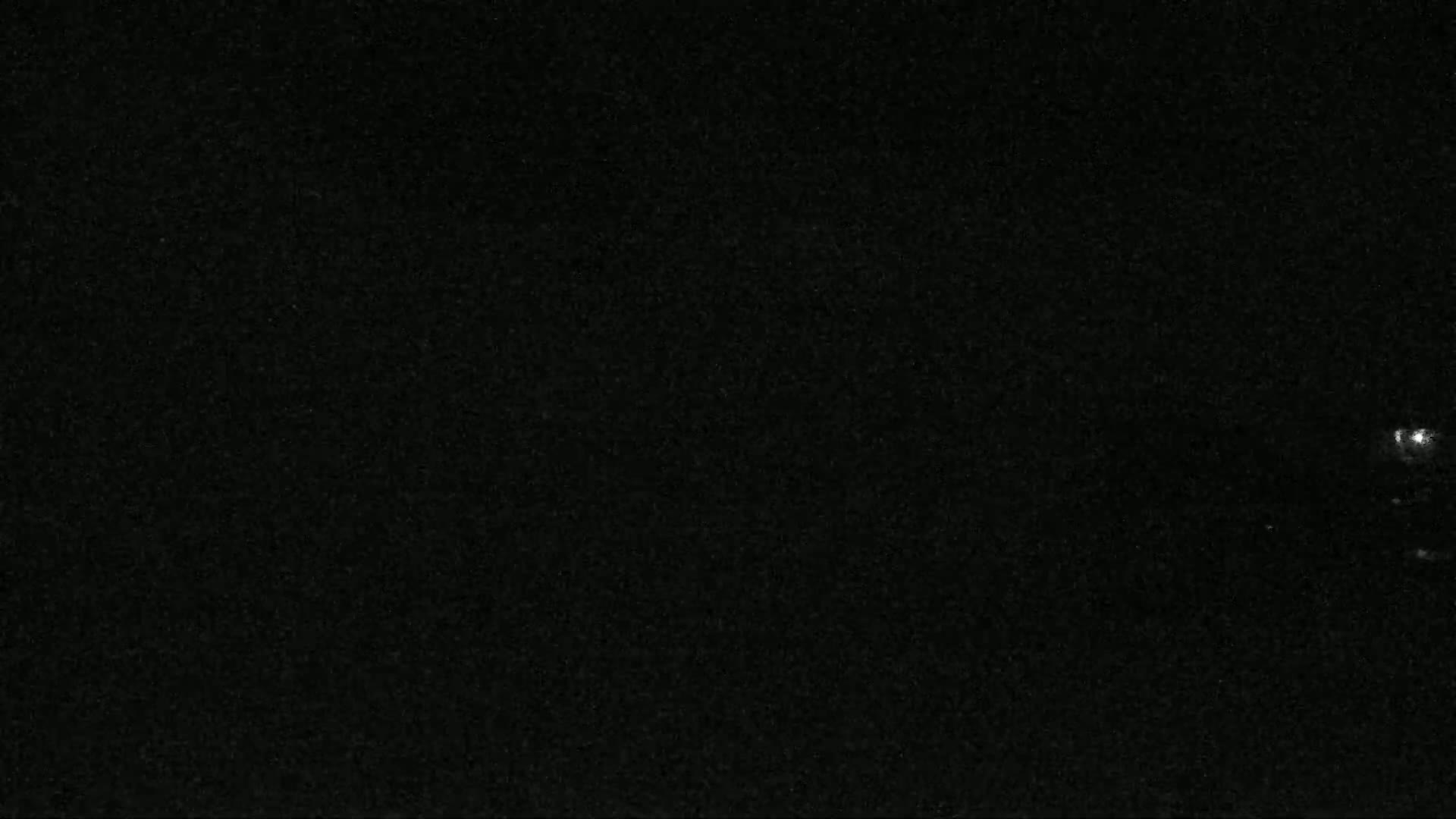 A dark, nighttime scene shows a few faint lights in the distance.