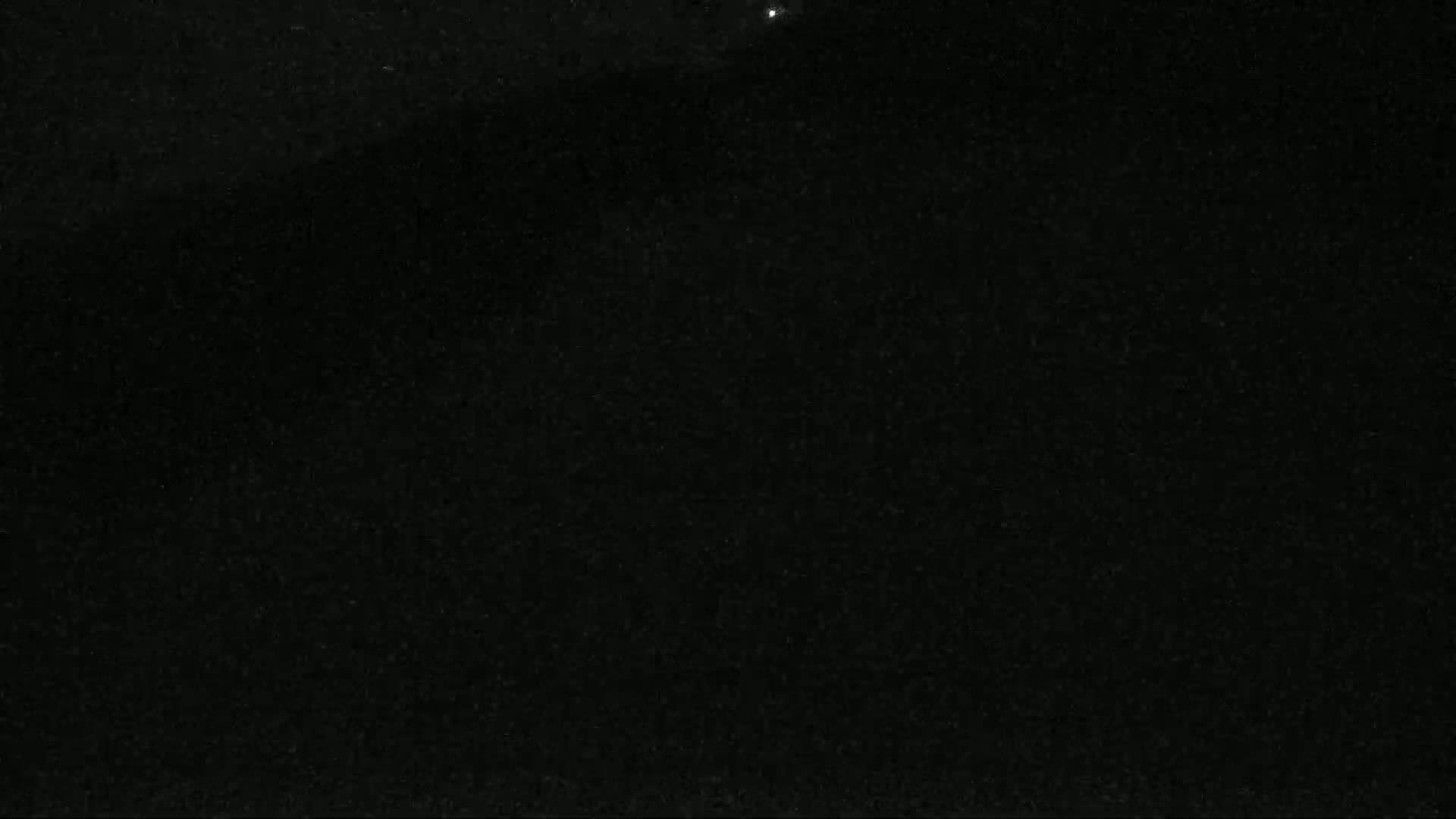 A dark, grainy image shows a mostly black night sky with a few faint, indistinguishable specks of light.