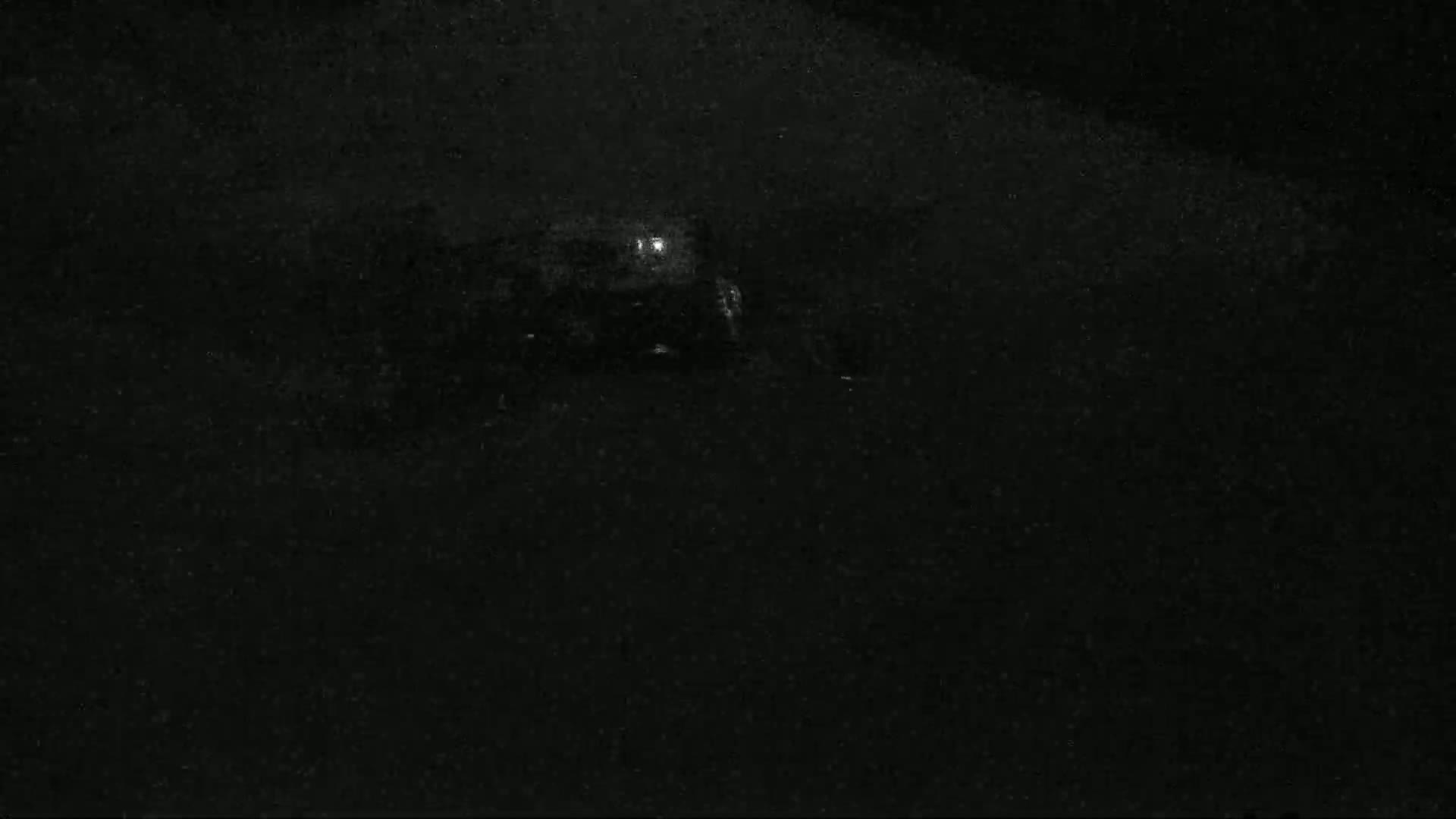 A dimly lit, dark scene at night shows a vehicle with a single light on in the distance.