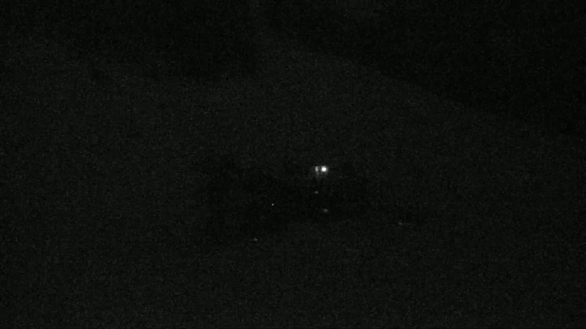 A nighttime image shows a few faint lights in the dark.