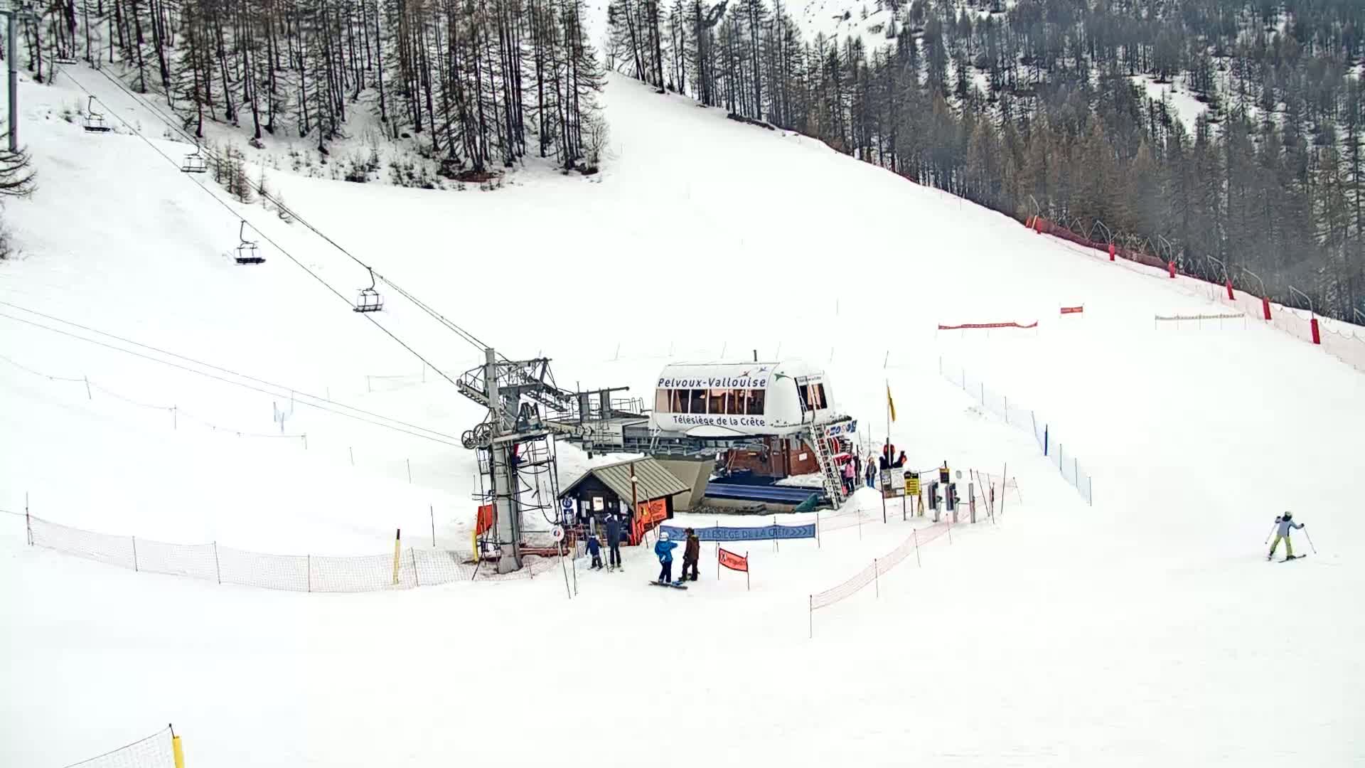 A chairlift and skiers are visible on a snowy ski slope surrounded by a coniferous forest.