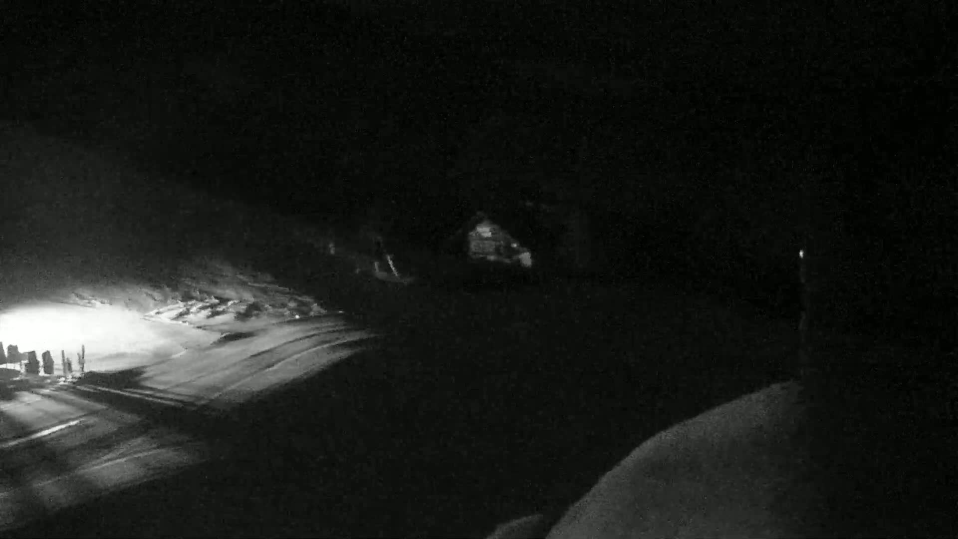 A snow-covered landscape is visible at night, illuminated by a light source in the lower left, with a dark structure faintly visible in the mid-ground.