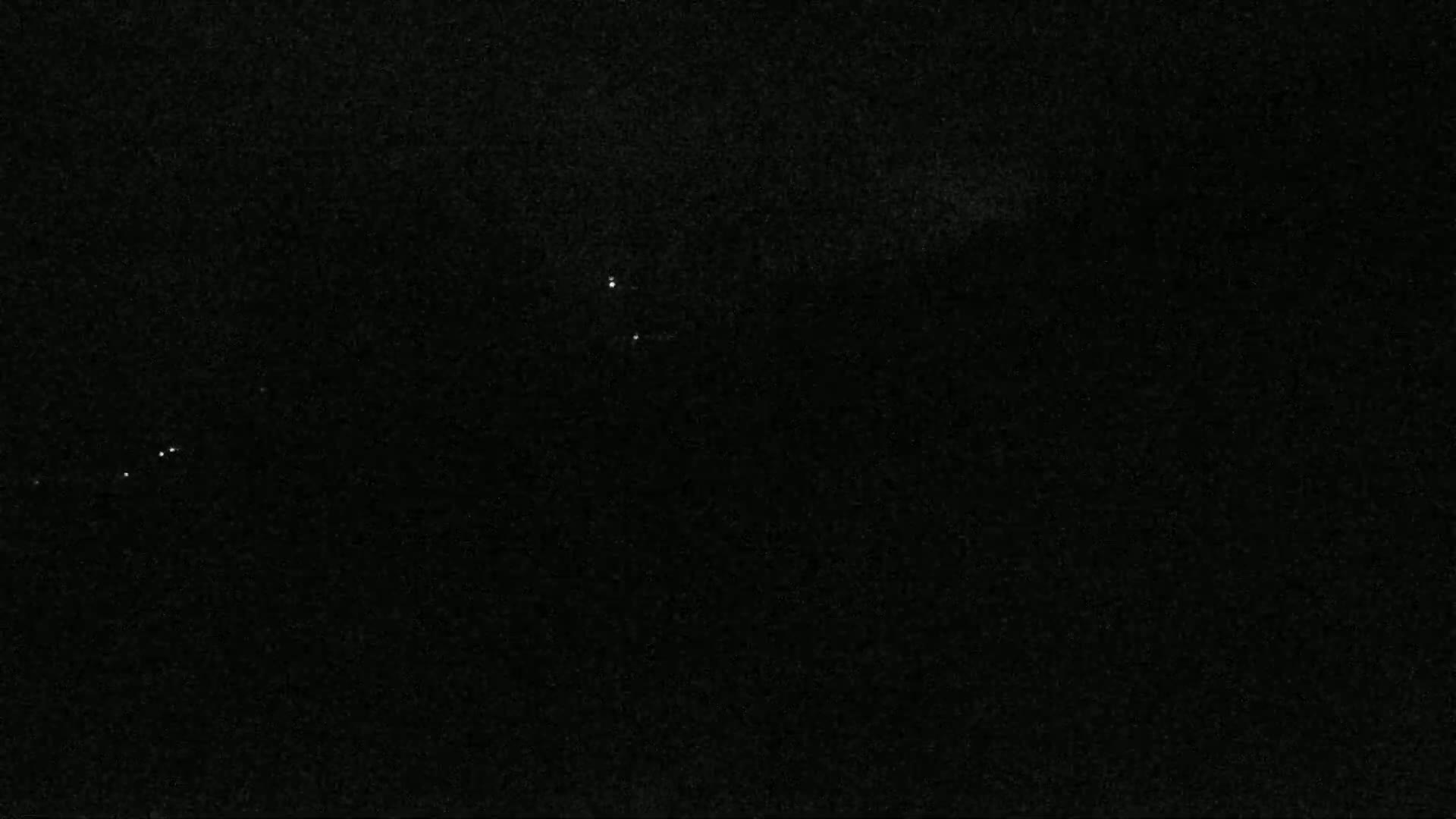 A dark, nighttime scene shows a few faint lights in the distance against a mostly black sky.