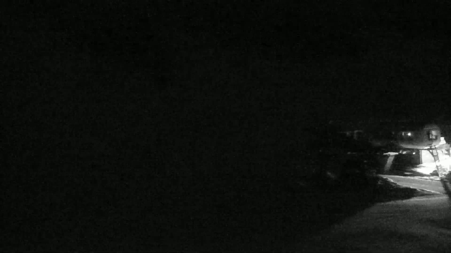A nighttime, low-light image shows a dark street and the dimly lit sides of houses.