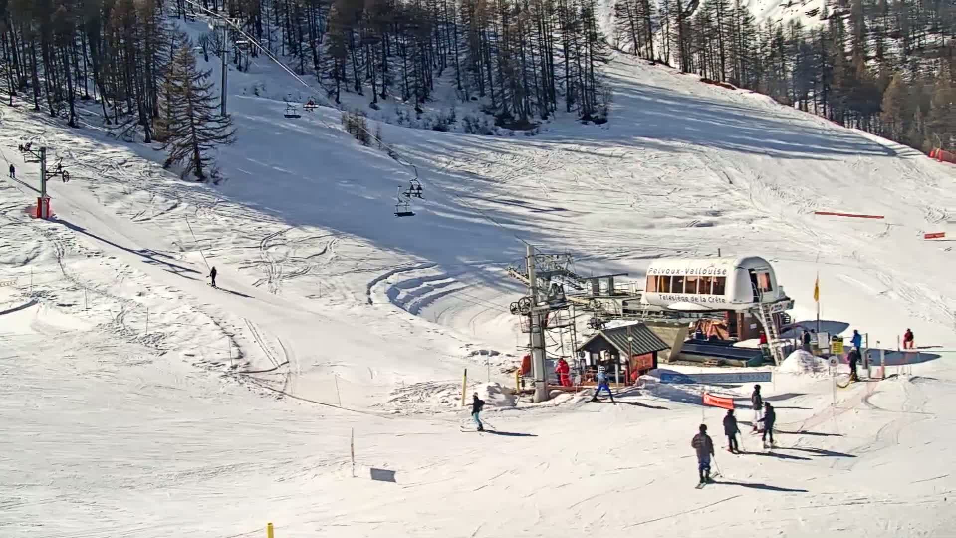 A sunny ski slope with several skiers and chairlifts, showing tracks in the snow.