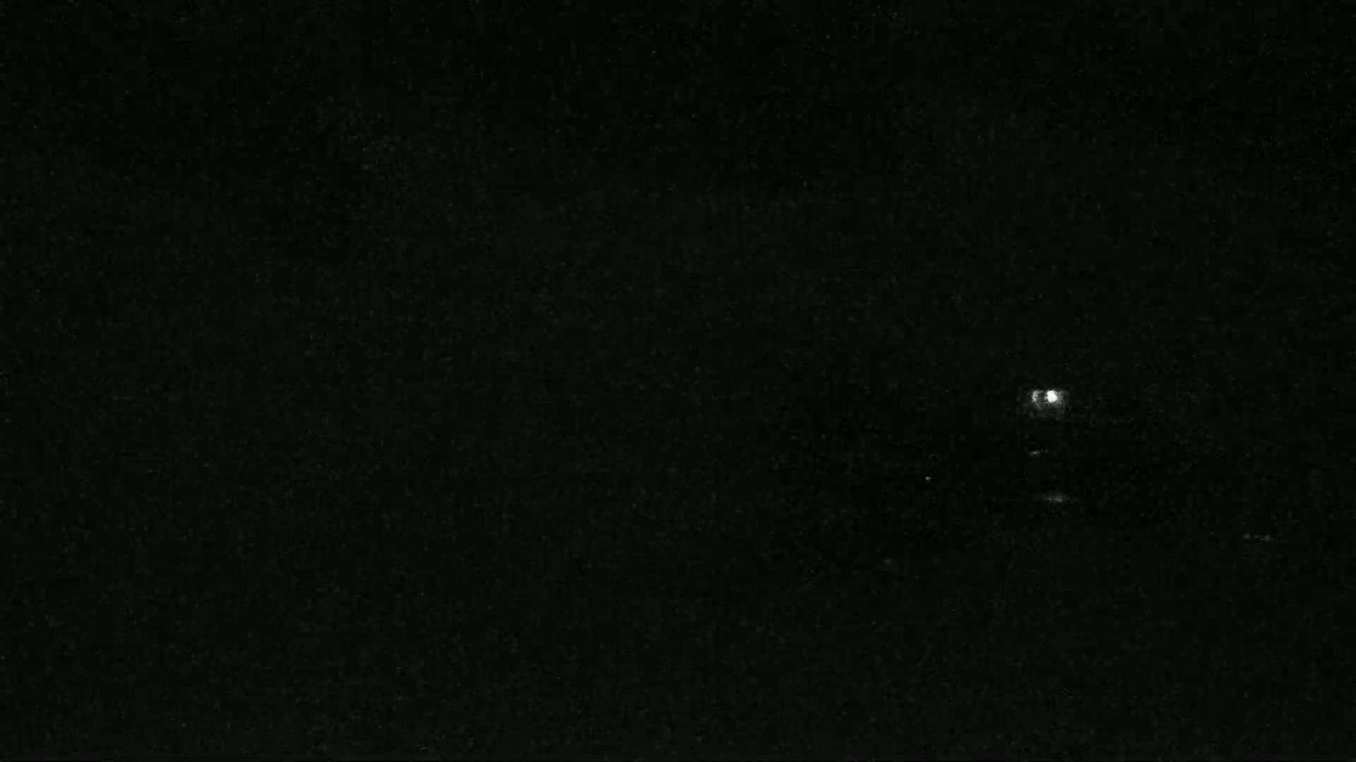 A nighttime image shows a bright light in the distance against a dark, speckled sky.
