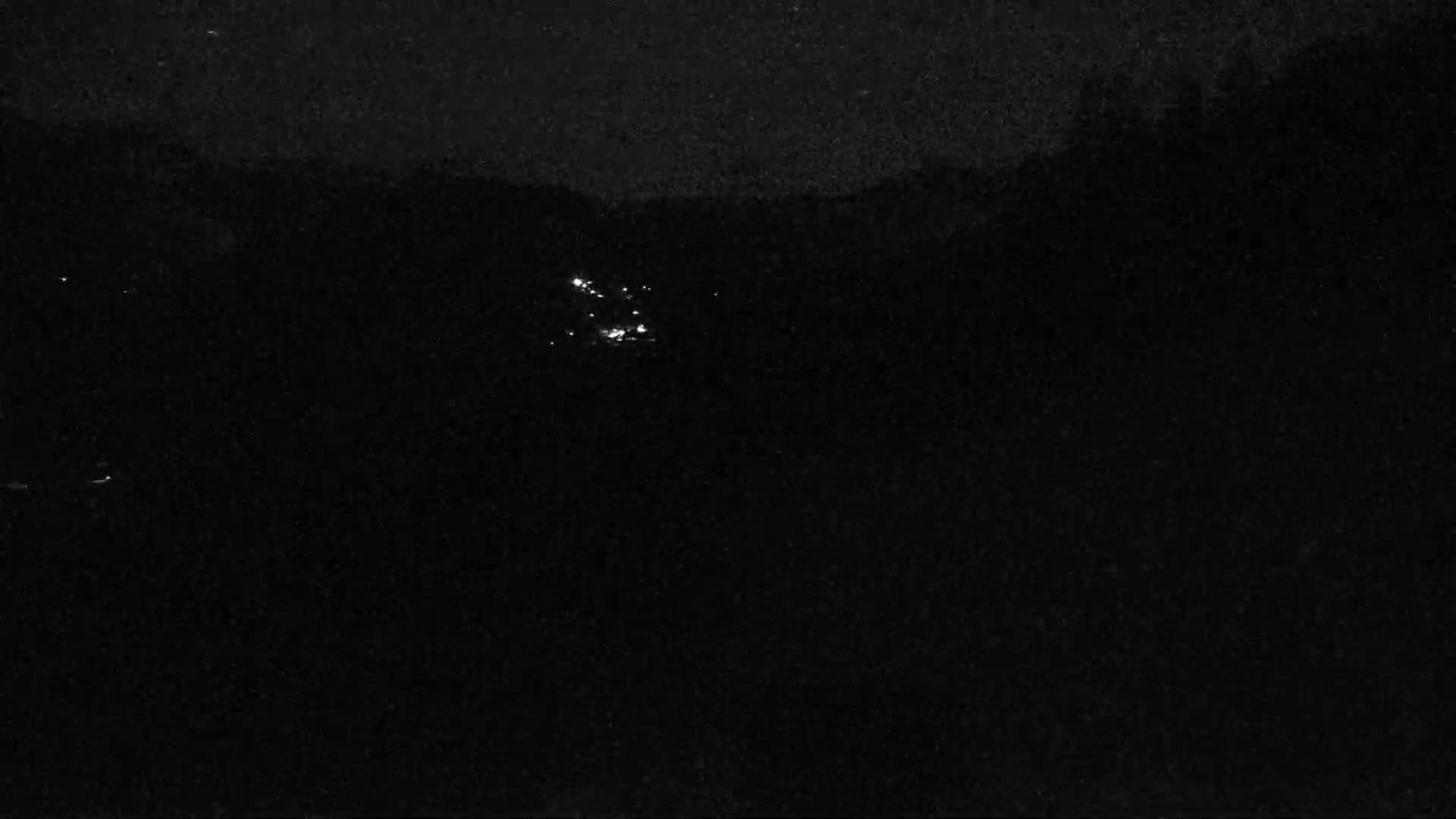 A nighttime, dark landscape with a few faint lights visible in the distance.