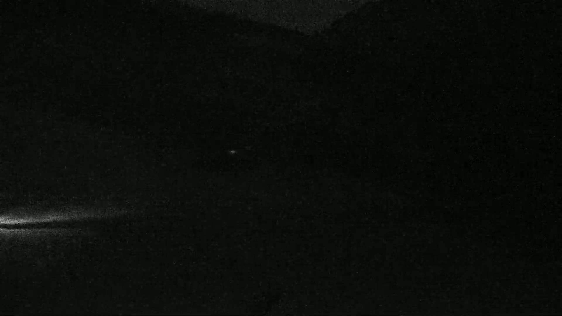 A nighttime, low-light image shows a faint light source at the bottom left, with a dark, possibly mountainous, background.