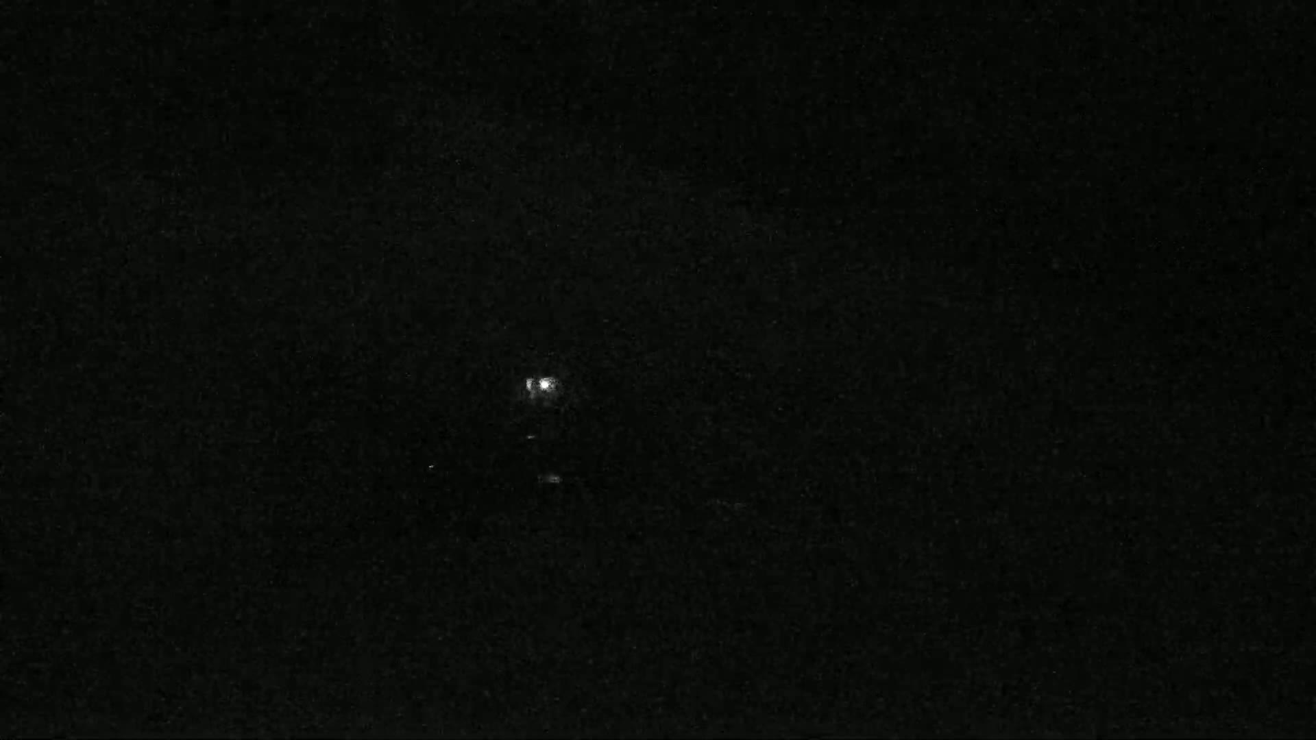 A dimly lit, dark scene at night shows a single light source in the distance.