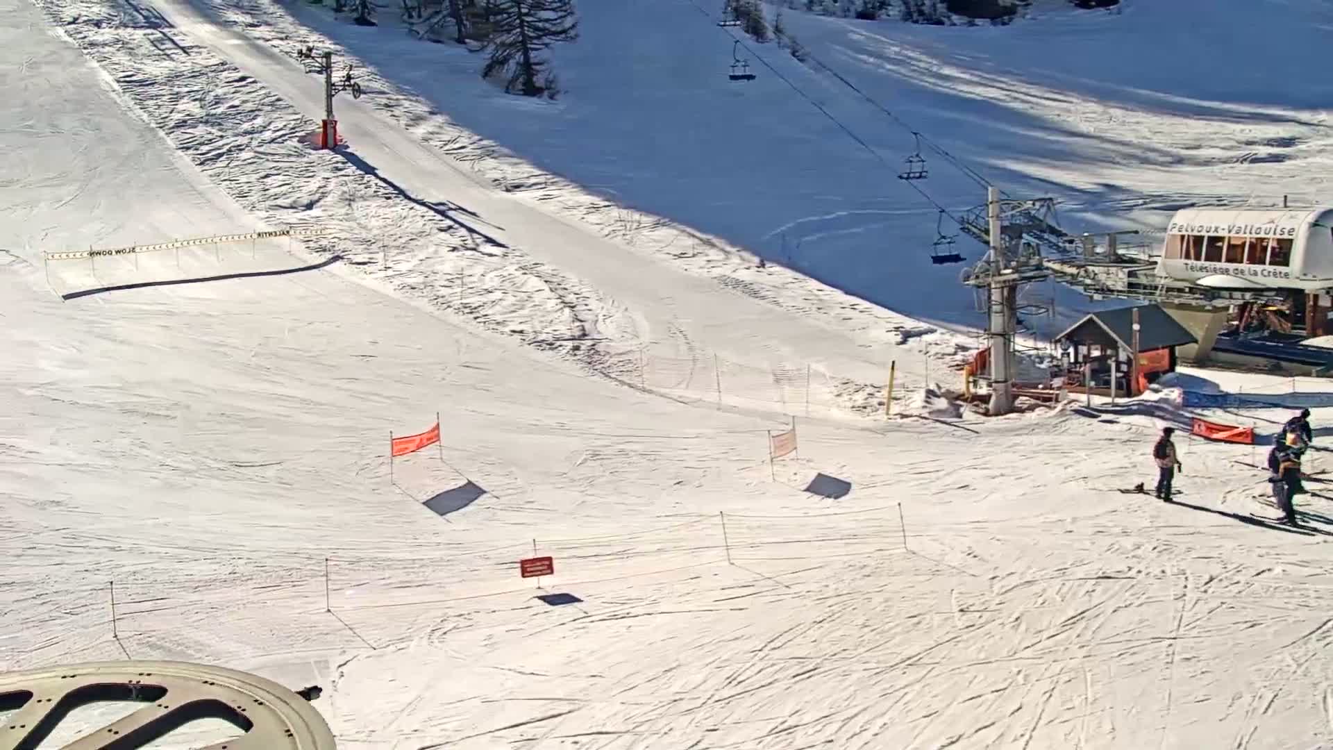 A sunny ski slope with a chairlift and several skiers near a lift station.