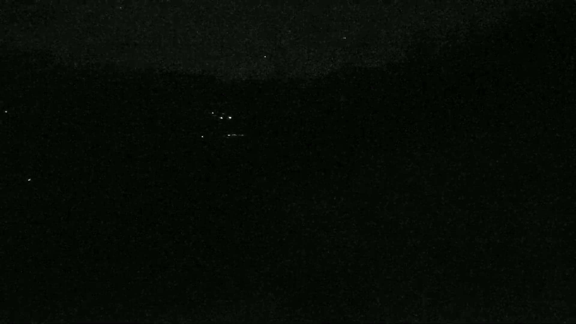 A nighttime image shows a dark, possibly overcast sky with a few faint lights visible in the distance.