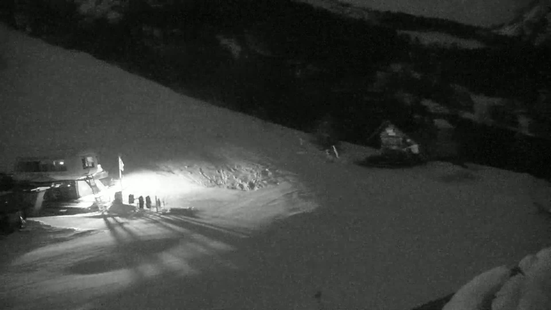 A snowcat is parked near a group of people at the bottom of a snow-covered slope at night.