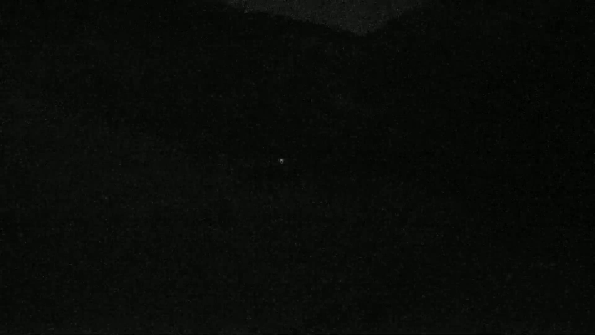 A single, faint white light is visible against a dark, speckled background.