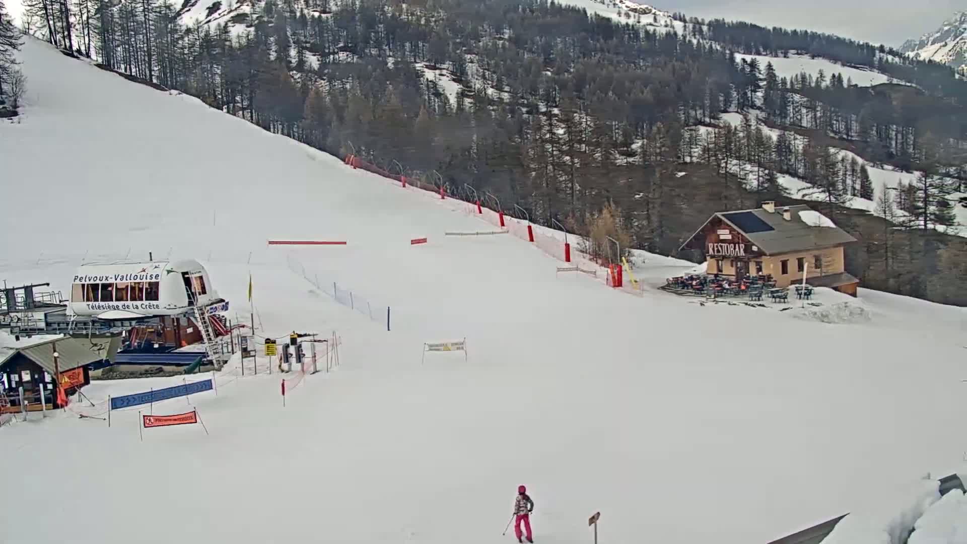 A snowy ski slope with a chairlift, a small restaurant, and a lone skier is visible under an overcast sky.
