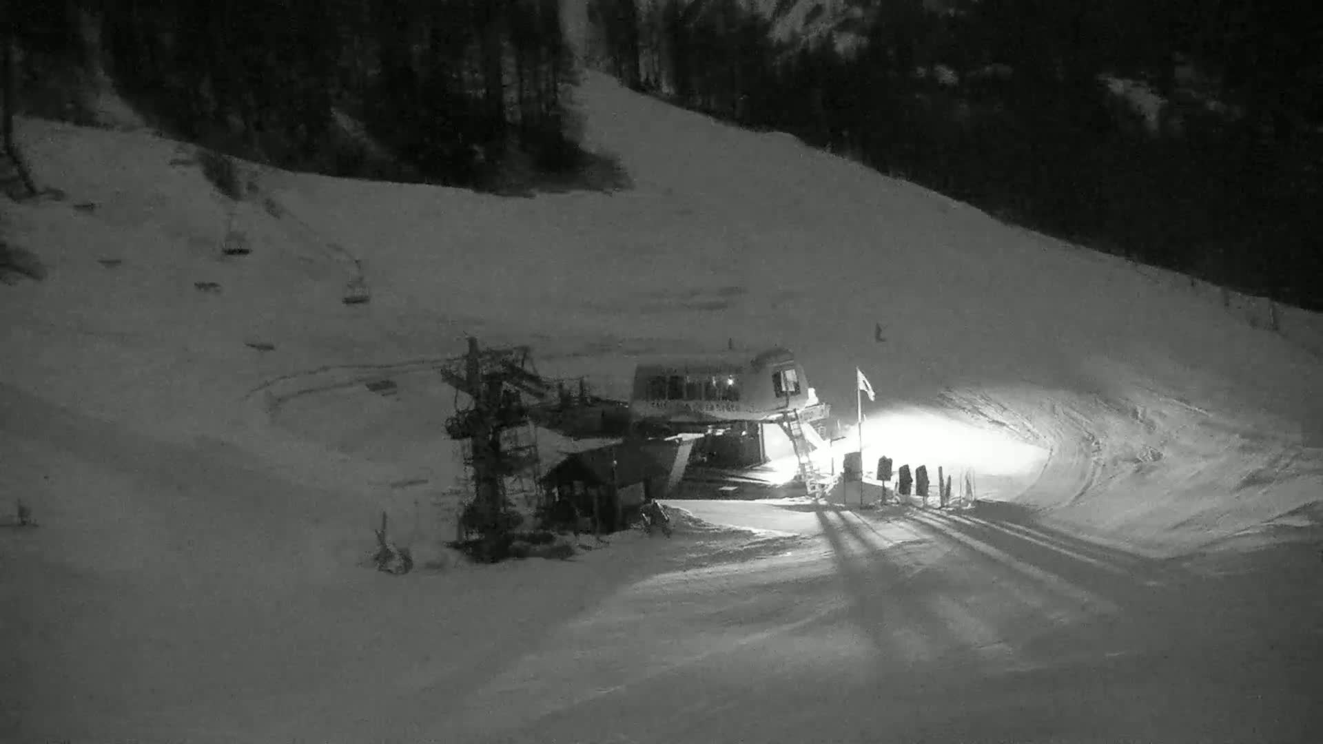 A ski lift and a small building are illuminated at night on a snow-covered slope under dark skies.