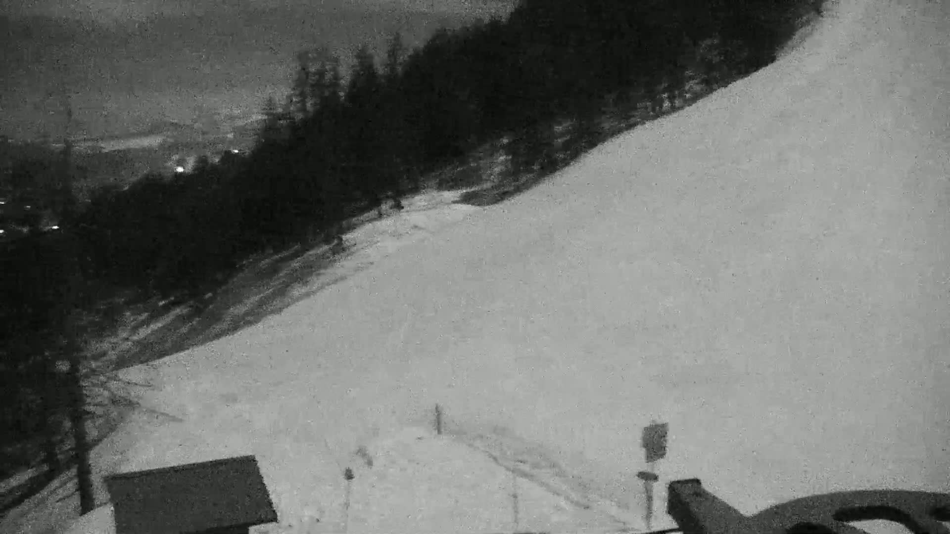 A snow-covered hill at night, viewed from a low vantage point, with a dark forest in the background.