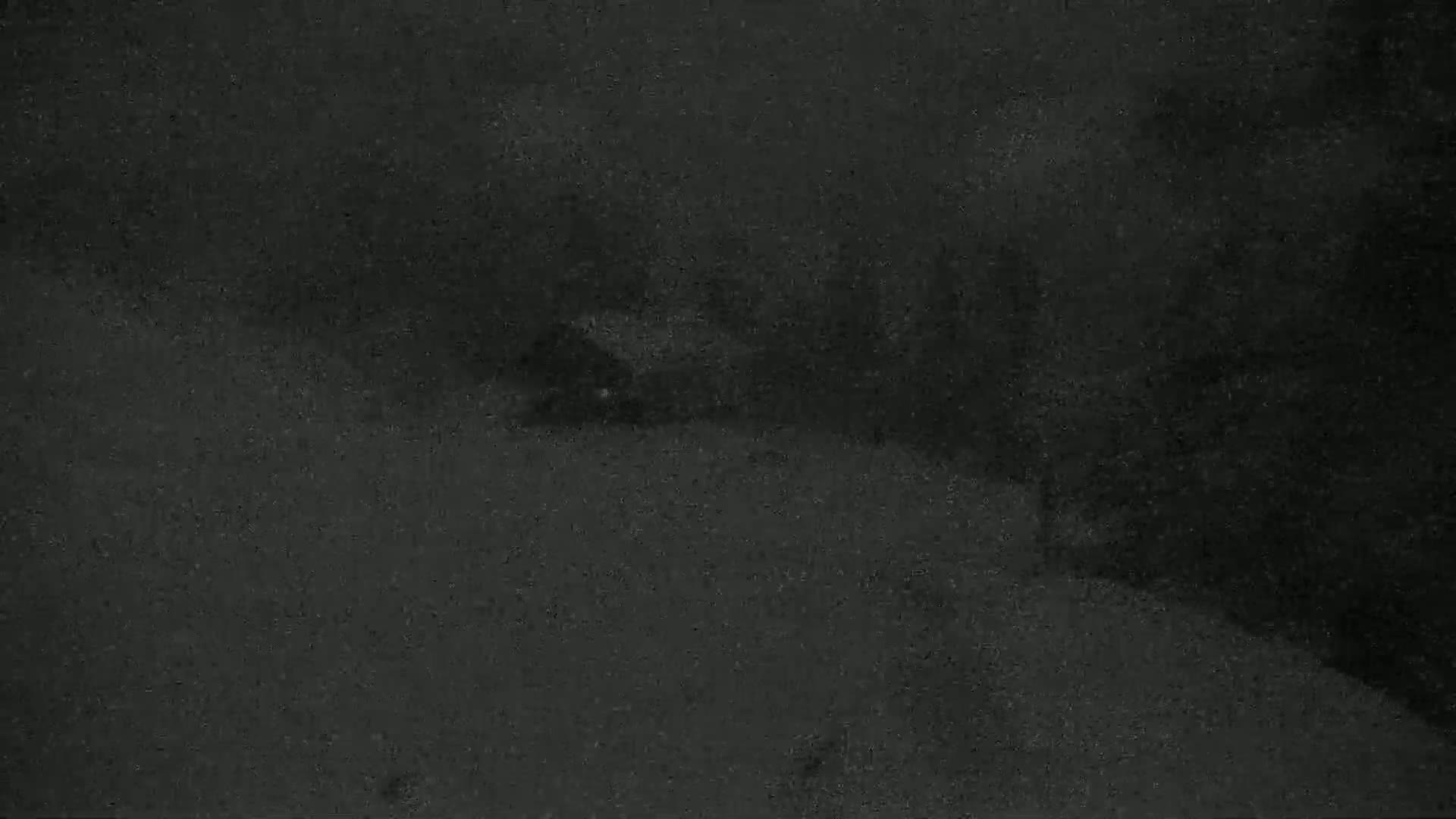 A dimly lit, dark gray landscape is shown, possibly at night, with a suggestion of a structure or object in the middle distance.