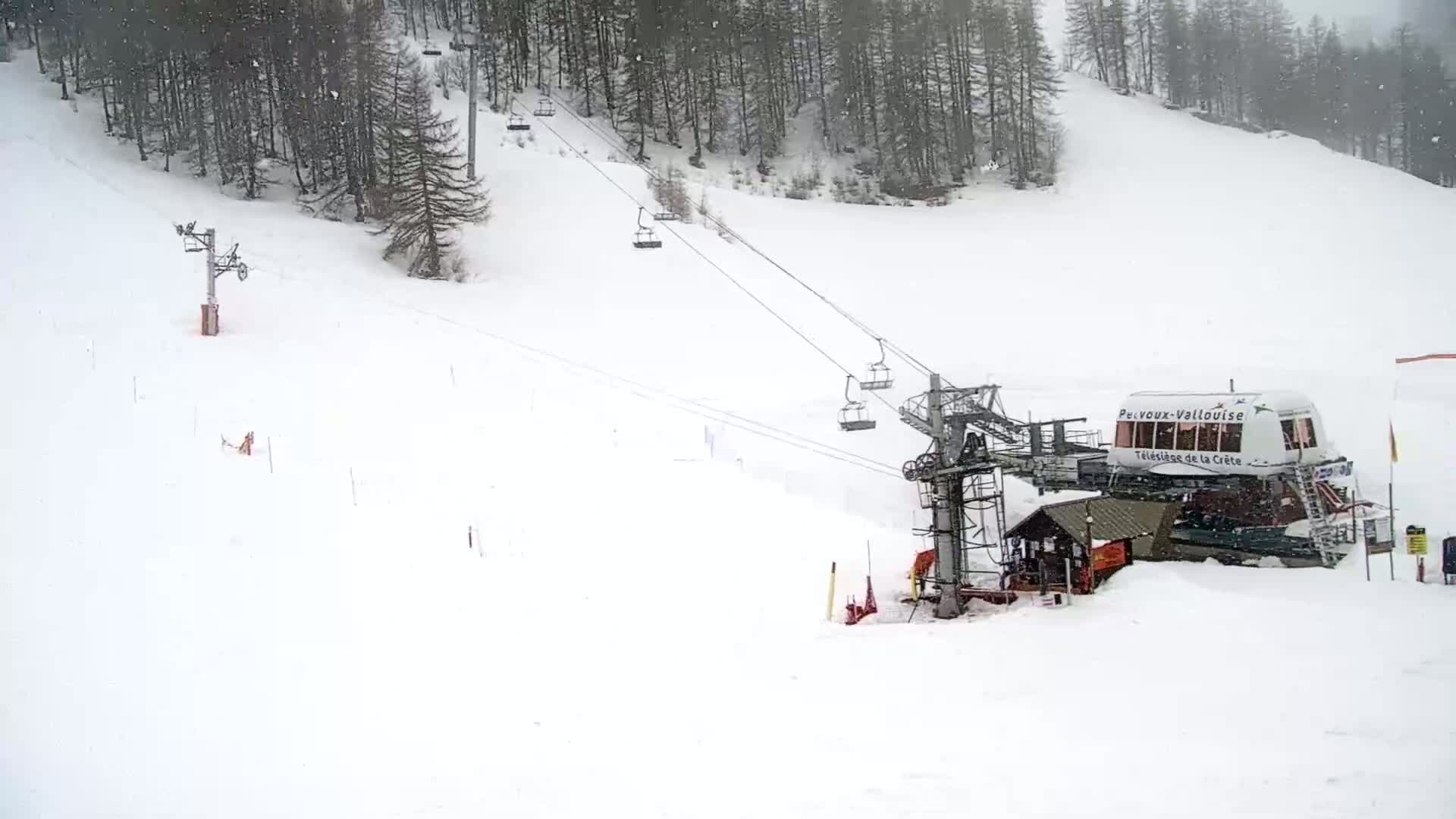 A snow-covered ski slope with a chairlift and a snow-covered lift station, in snowy conditions.