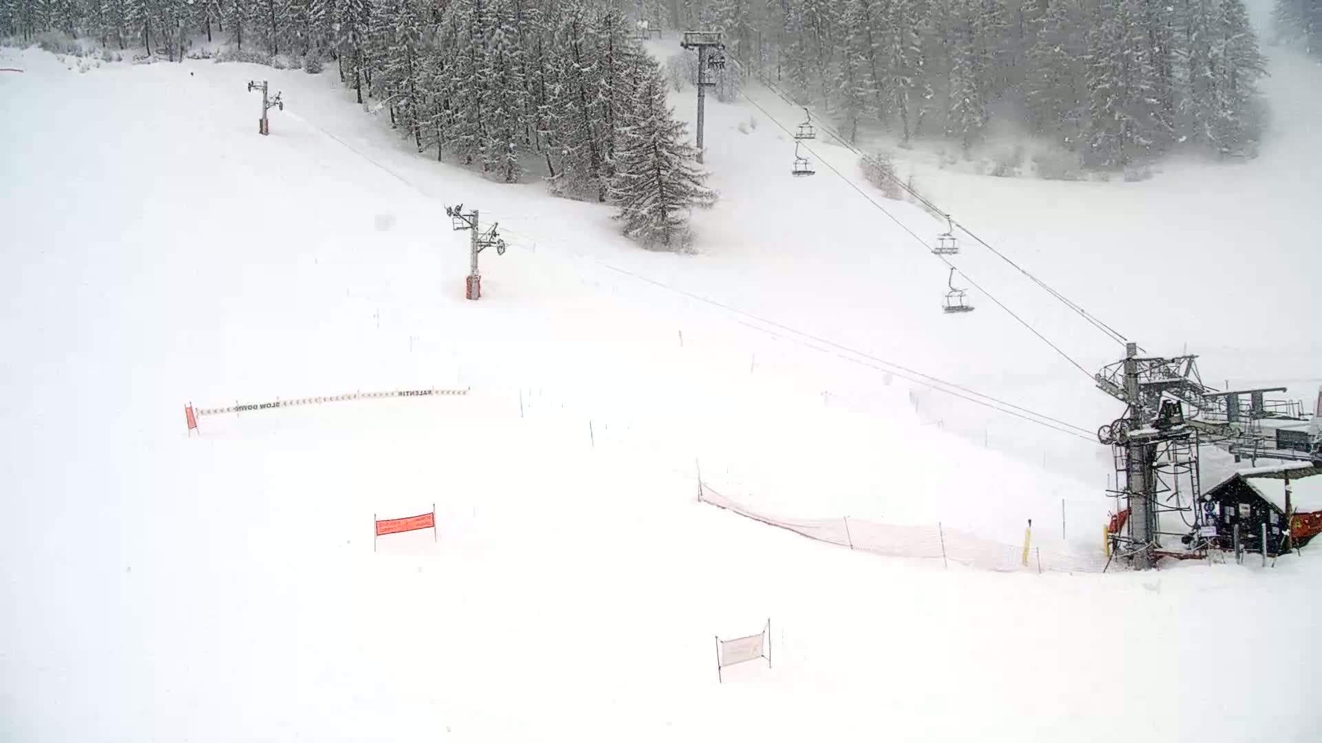 A snow-covered ski slope with several chairlifts and snow fences, under snowy conditions.