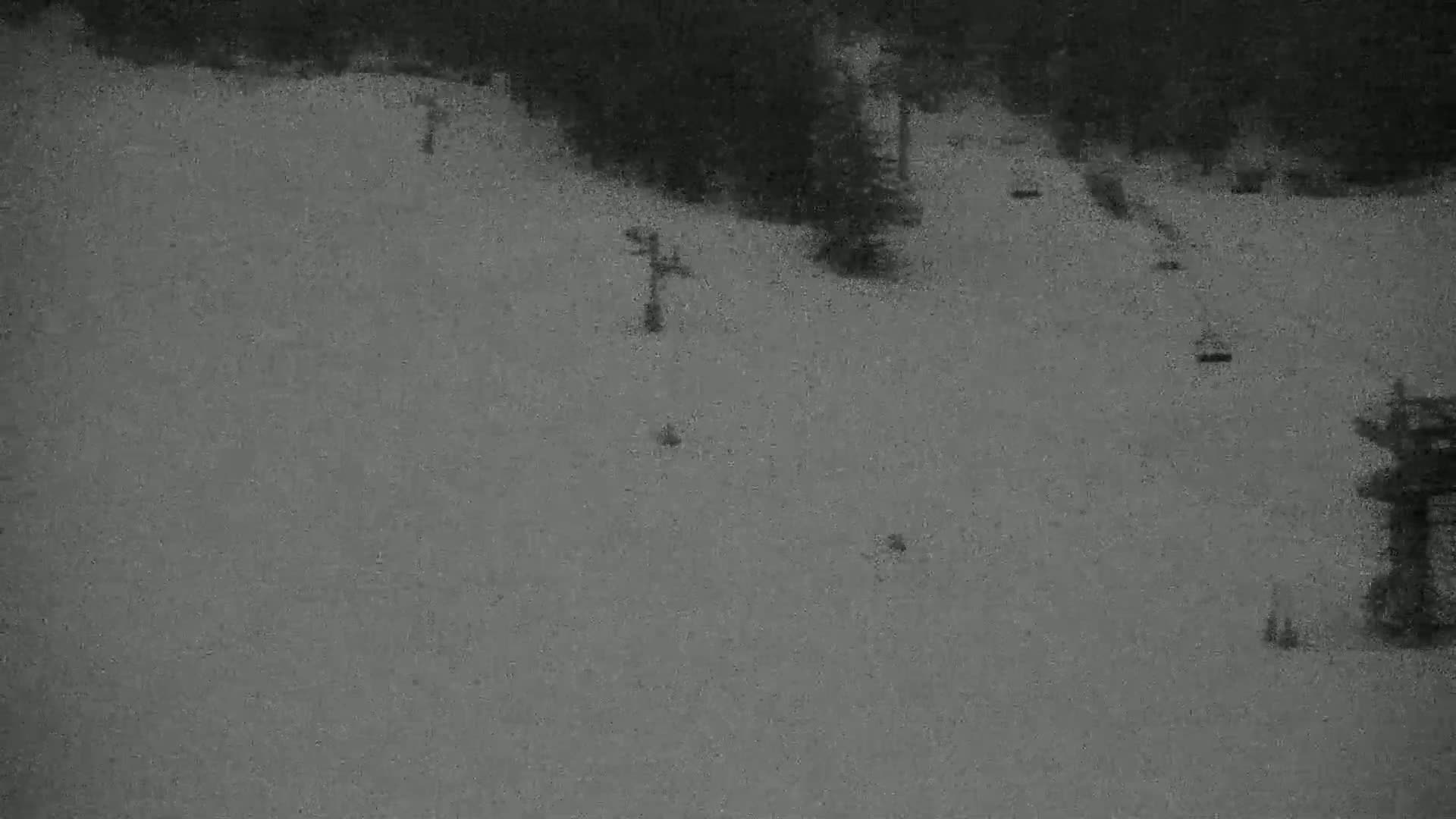 A snow-covered ski slope with several ski lifts and a few indistinct skiers is visible under nighttime or low-light conditions.