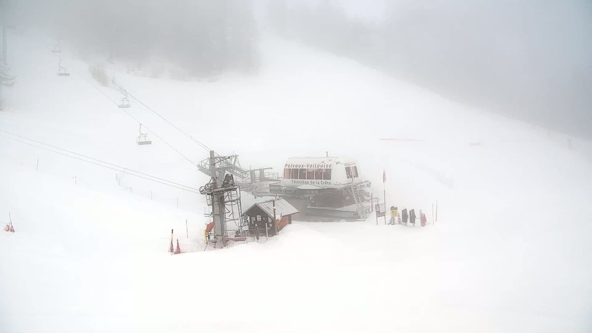 A ski lift station and empty chairlift are visible in a snow-covered landscape shrouded in heavy fog.