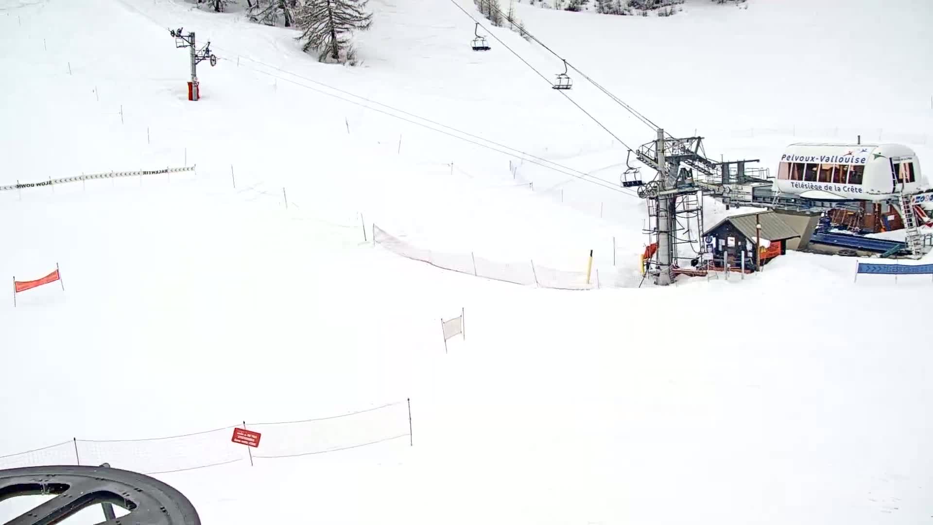 A snow-covered ski slope with a chairlift and safety nets is visible under overcast skies.