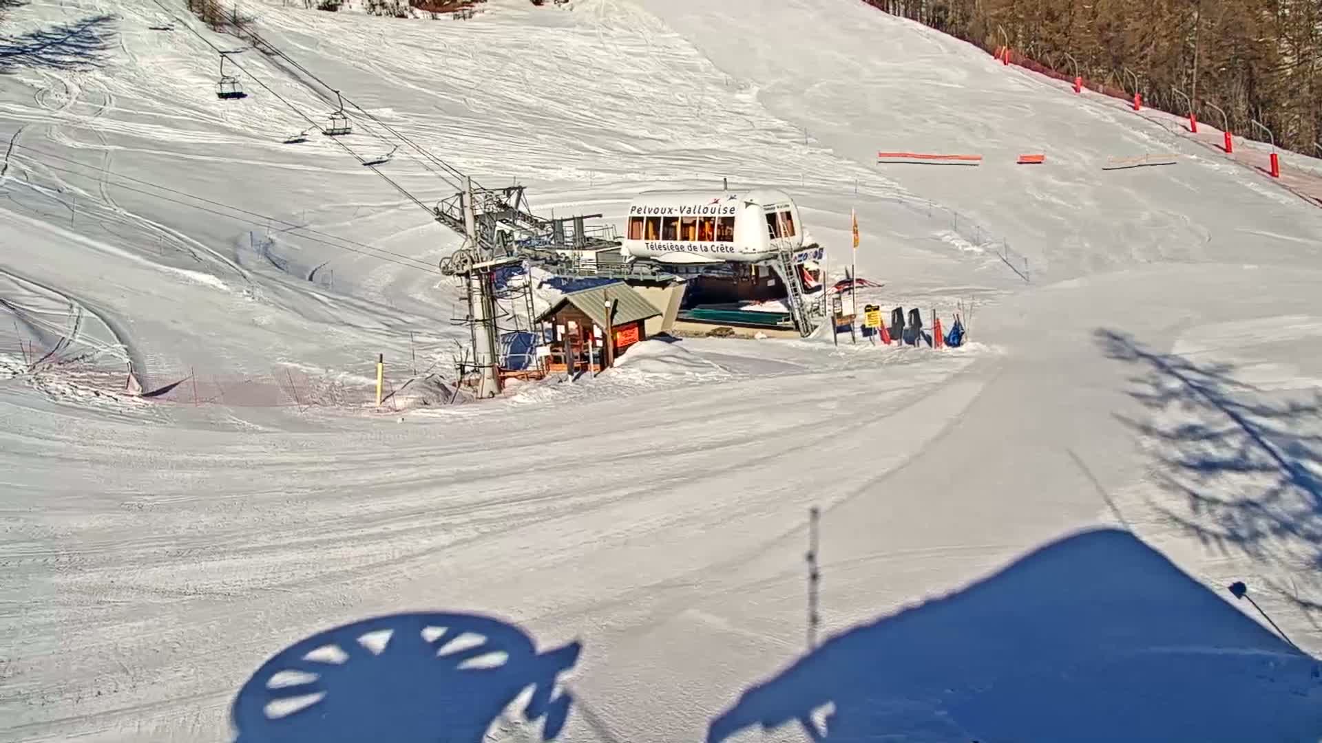 A ski lift station sits on a snow-covered slope on a sunny day.