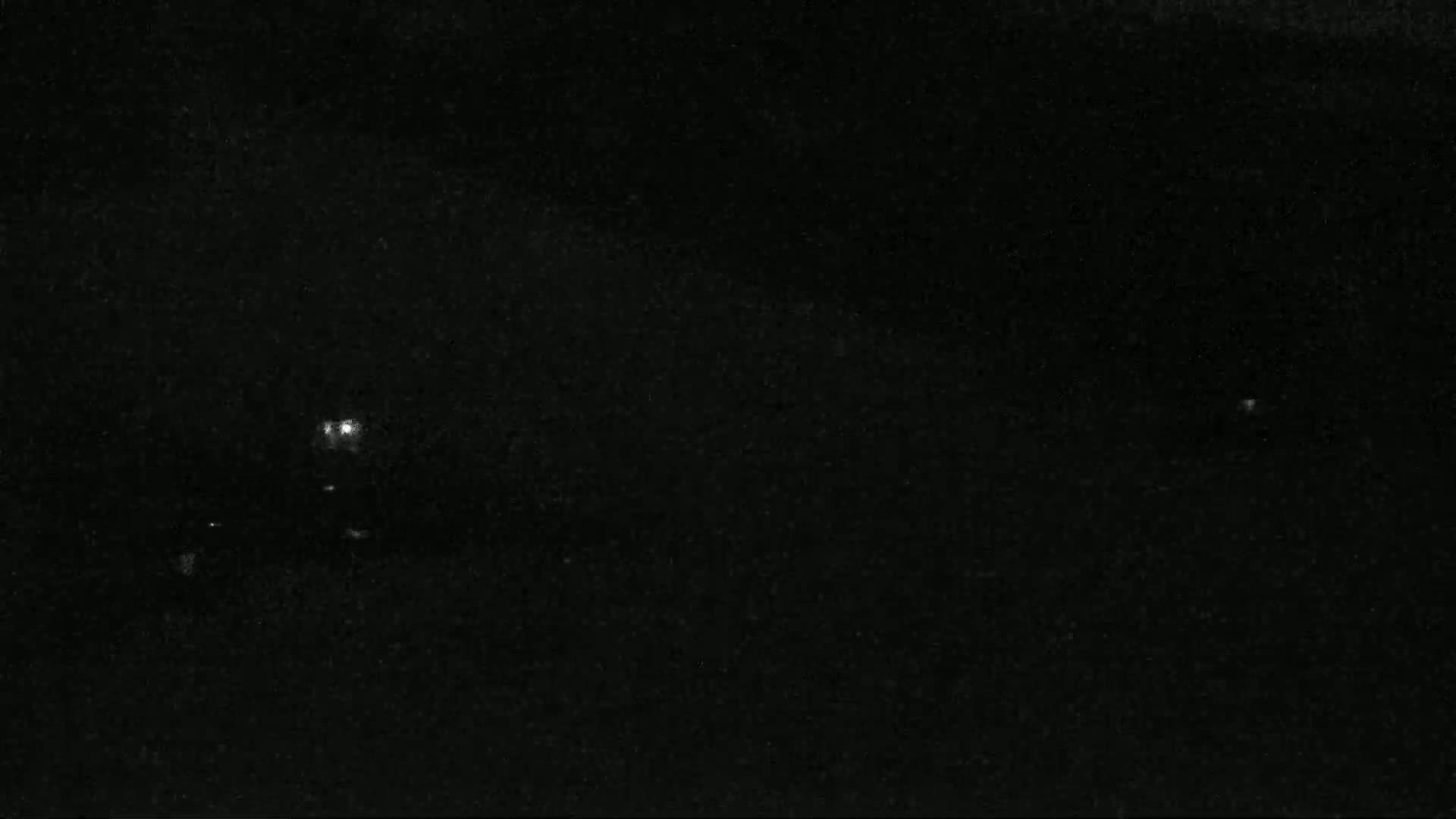 A dark, nighttime scene shows a few faint lights in the distance.