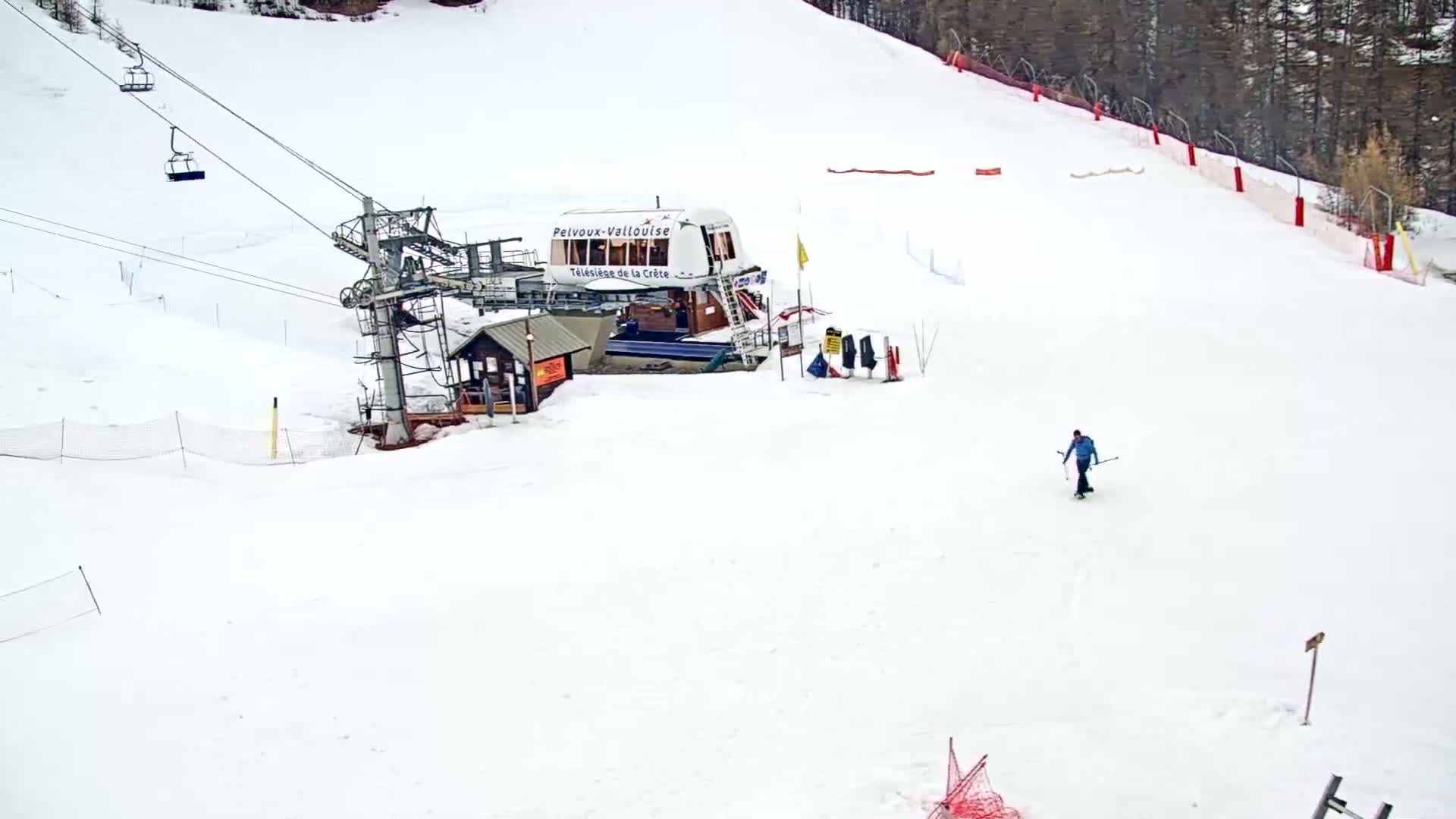 A snowy ski slope features a chairlift, a small building, and a lone skier.