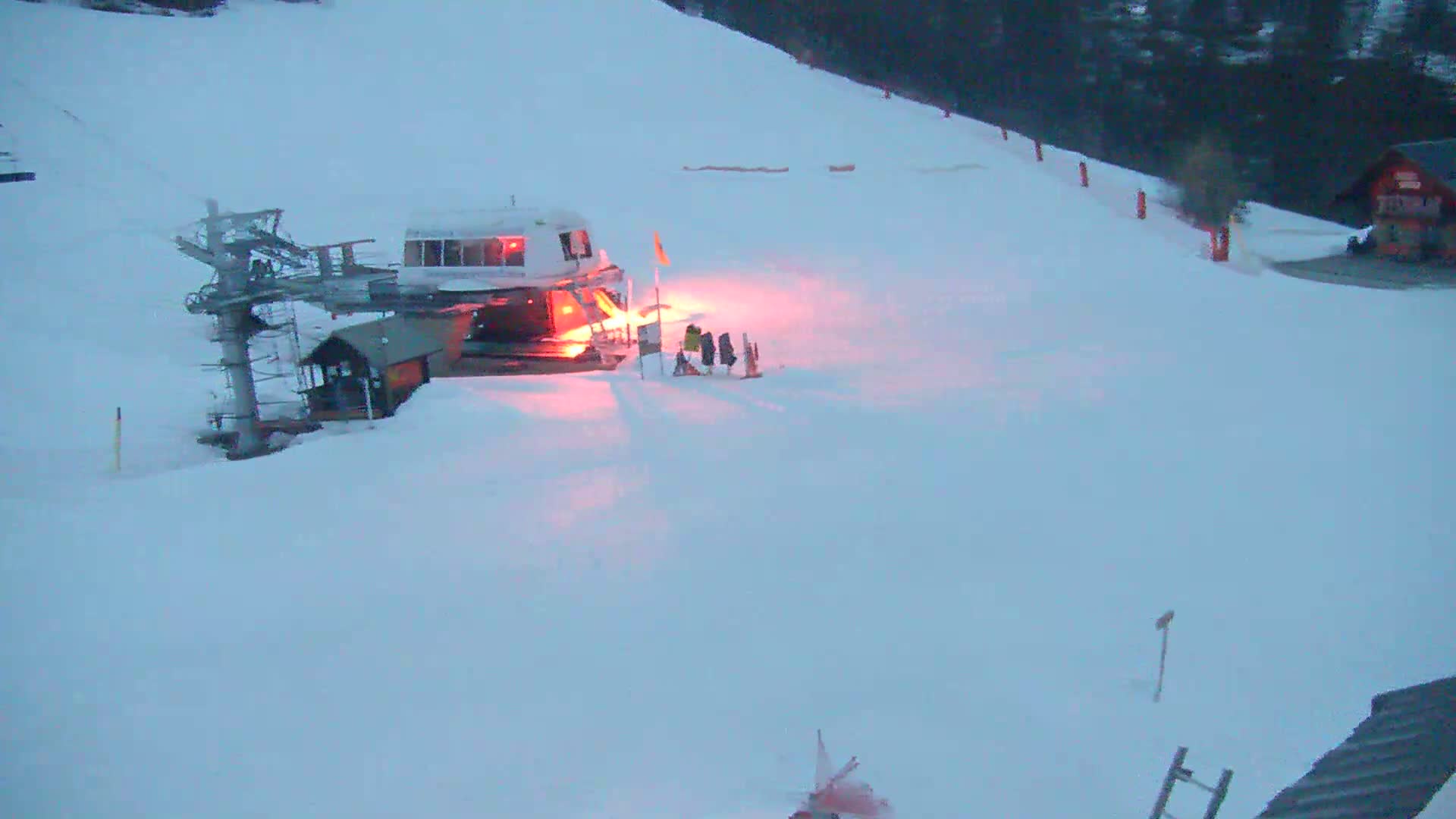 A ski lift and small building are covered in snow under a twilight sky.