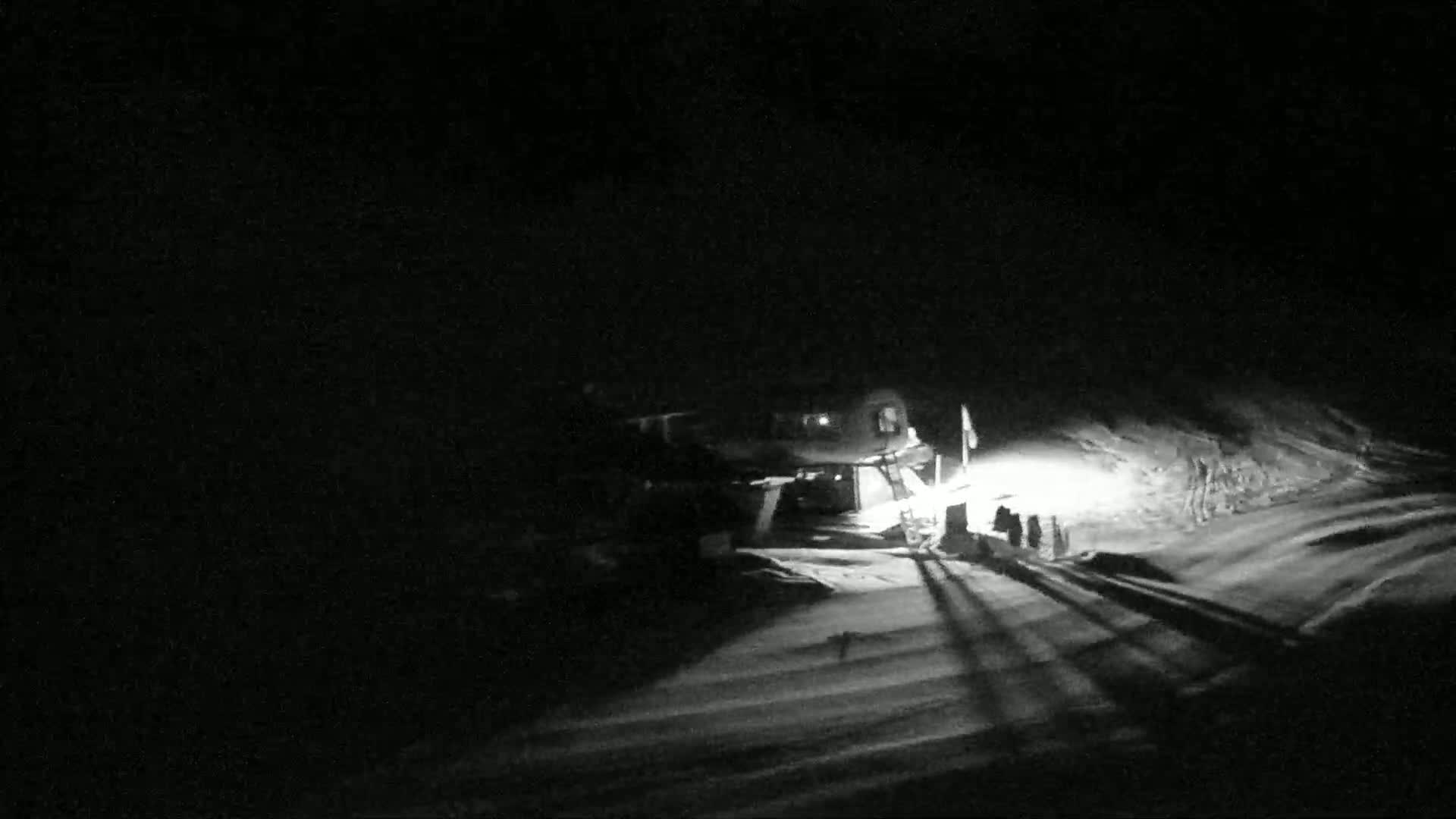 A snowcat is illuminated at night in a snow-covered area, casting long shadows.