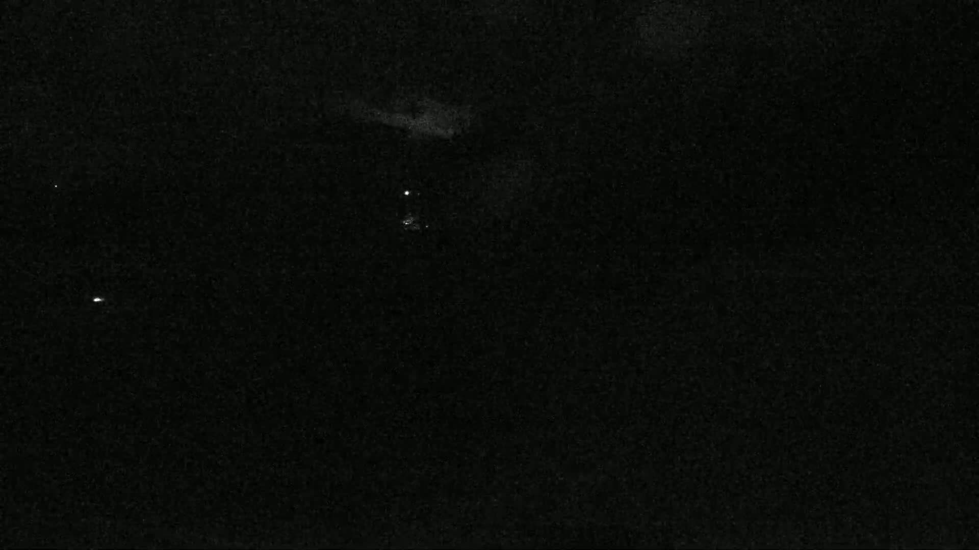 A nighttime, mostly dark image shows a few faint, small lights in the distance.