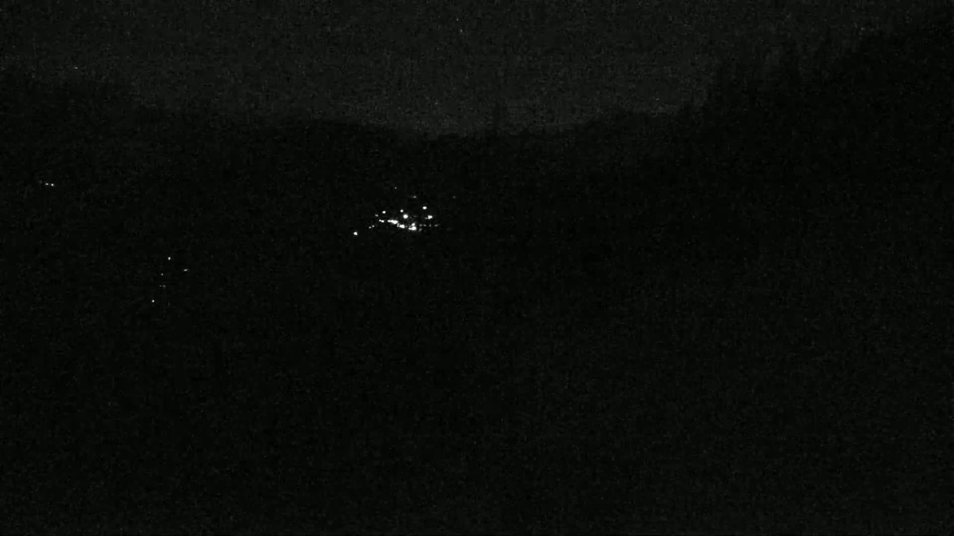 A nighttime long shot shows a cluster of small, bright lights in the distance against a dark, possibly cloudy sky.