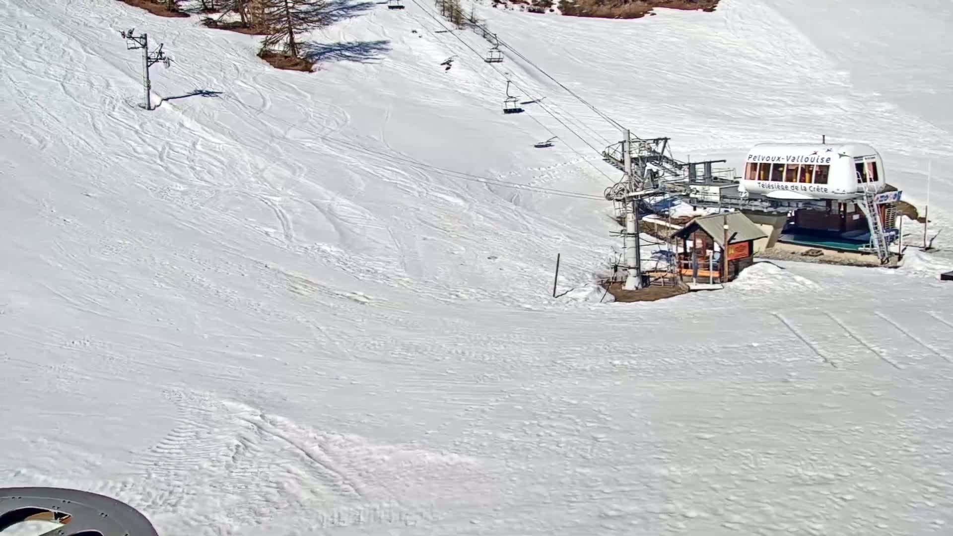 A ski lift terminal and chairlift are situated on a snow-covered slope on a bright, sunny day.