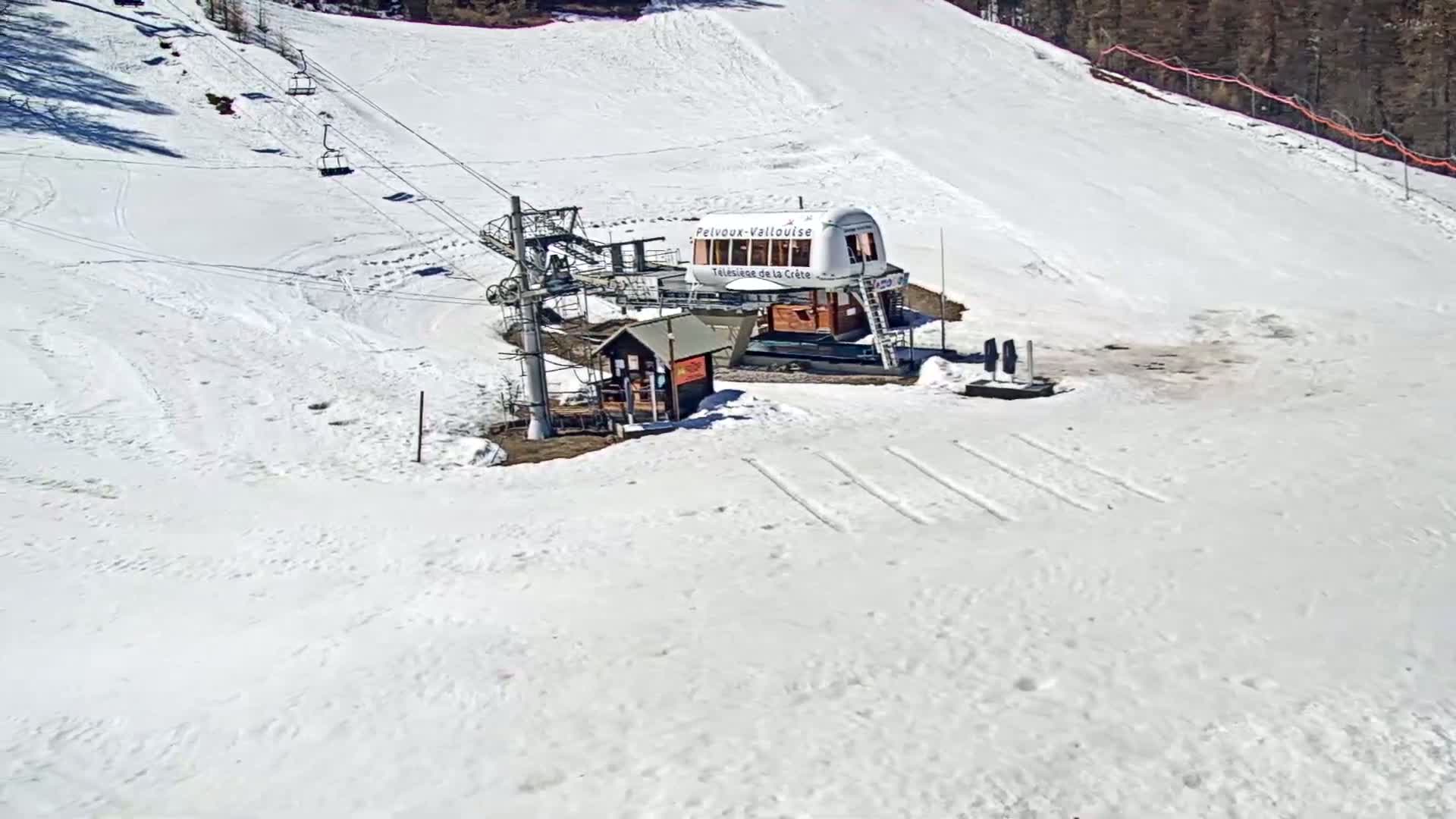 A snow-covered ski slope with a chairlift and a small building at the bottom, under bright, sunny conditions.