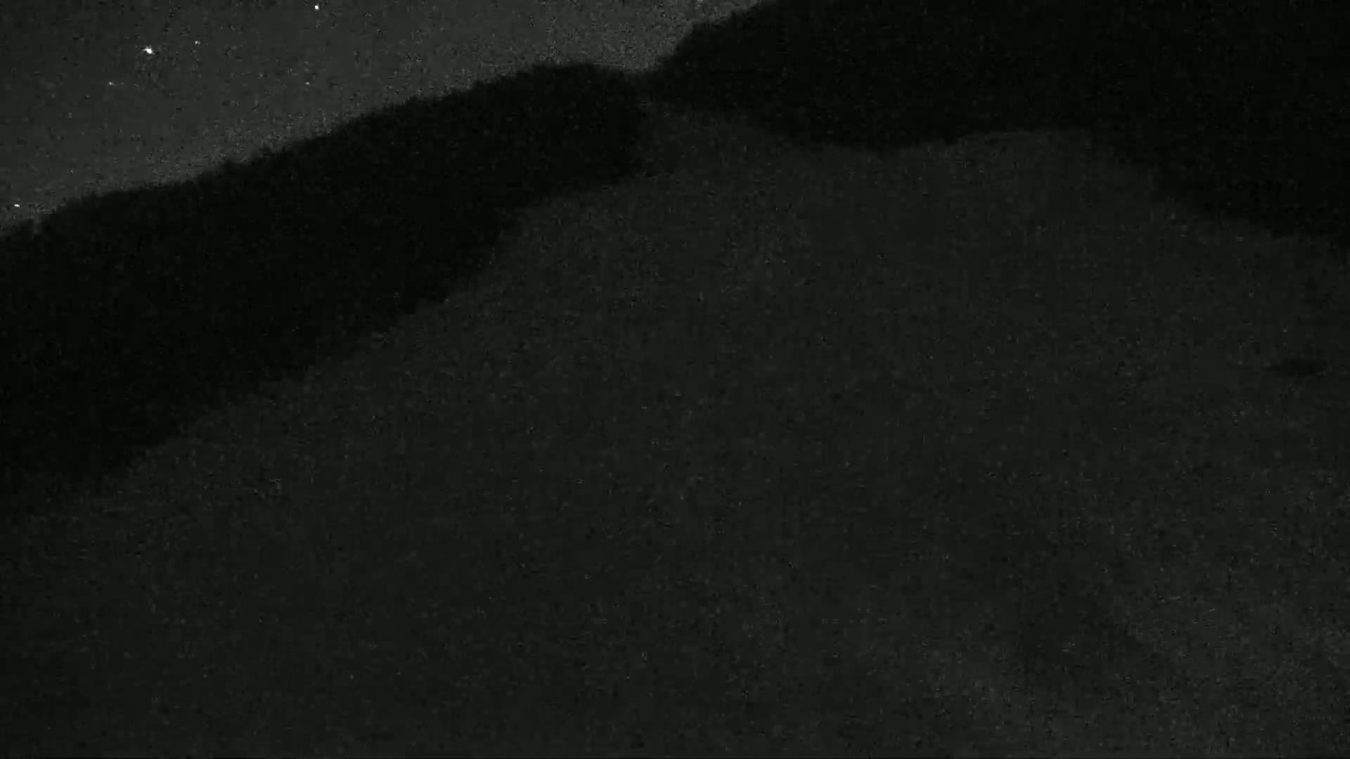 A dark, nighttime landscape shows a hill or mountain silhouetted against a starry sky.