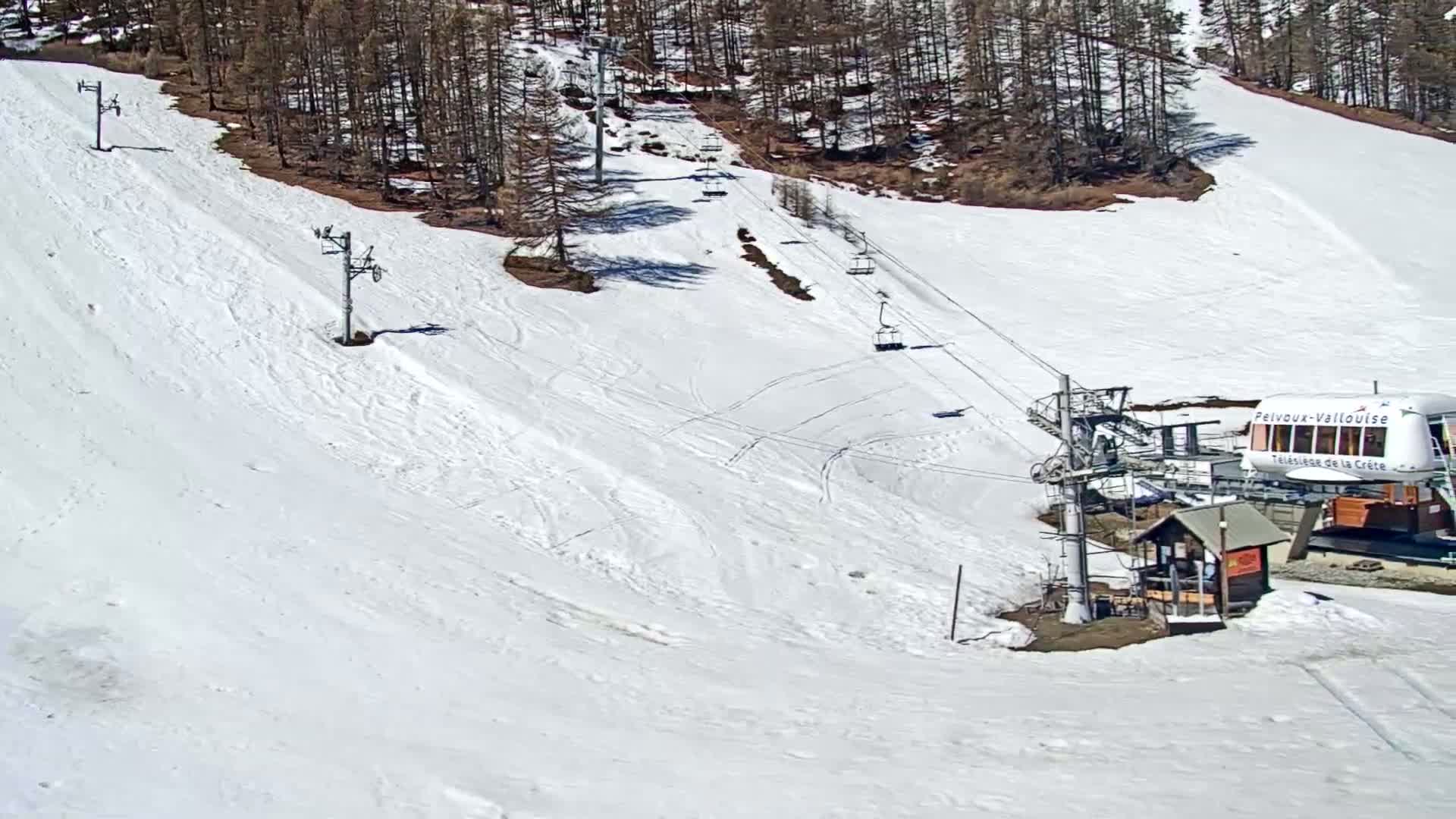 A snow-covered ski slope with a chairlift and a small building at the bottom, under sunny conditions.