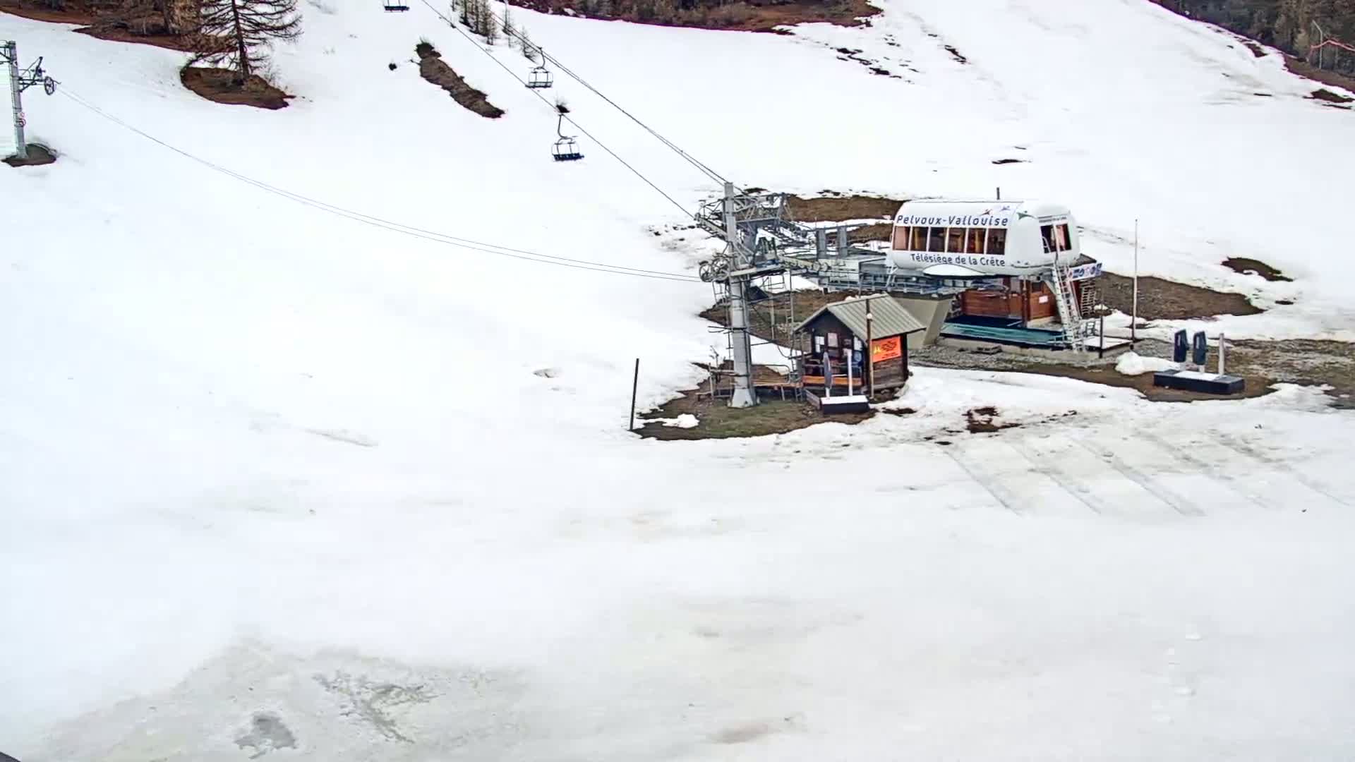 A snow-covered ski lift base station with a small building and chairlifts extending up a snowy hillside.