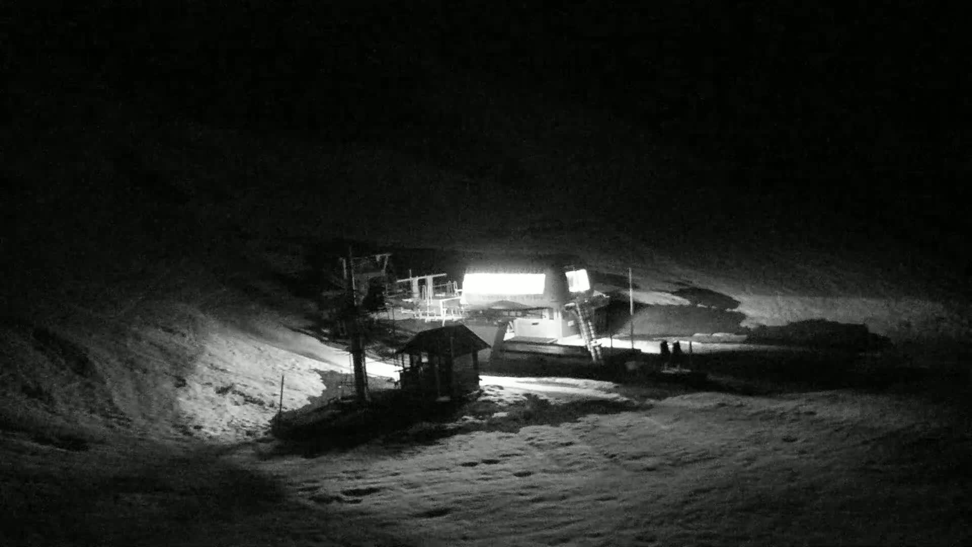 A brightly lit ski lift station sits on a snow-covered hill at night.