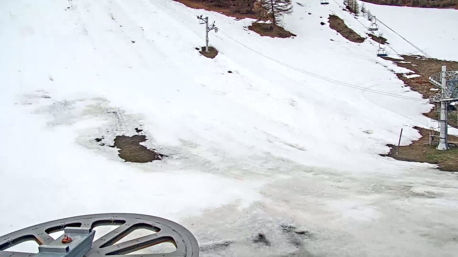 A snow-covered ski slope with several chairlifts and patches of bare ground is visible, partially melted snow and ice cover much of the ground.