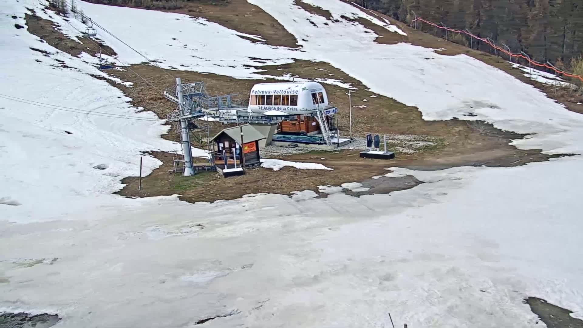 A ski lift station with a large white gondola sits partially in the melting snow on a hill.