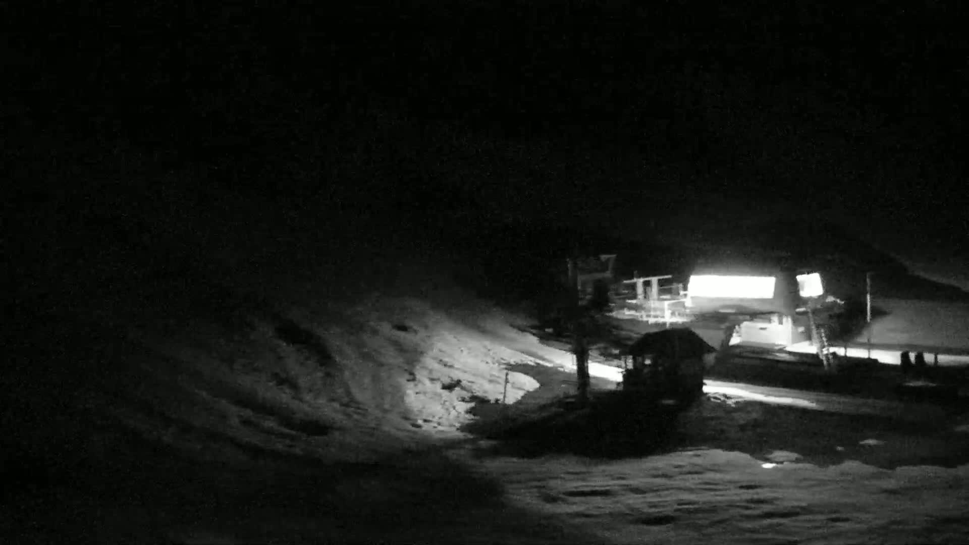 A snow-covered hill at night, illuminated by artificial lights near a building.