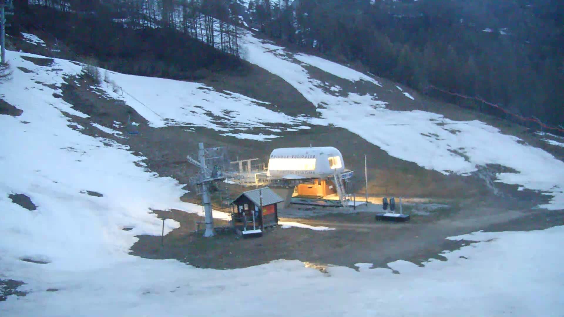 A ski lift station with patchy snow cover on a dark, possibly evening, hillside.