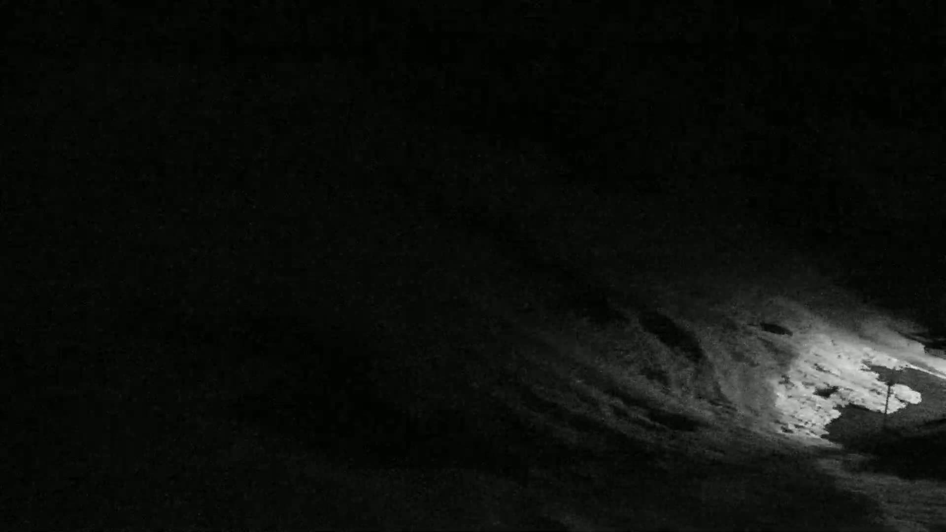 A dark, snowy scene is illuminated by a light source at the bottom right, showing a textured, uneven snow-covered surface under a night sky.