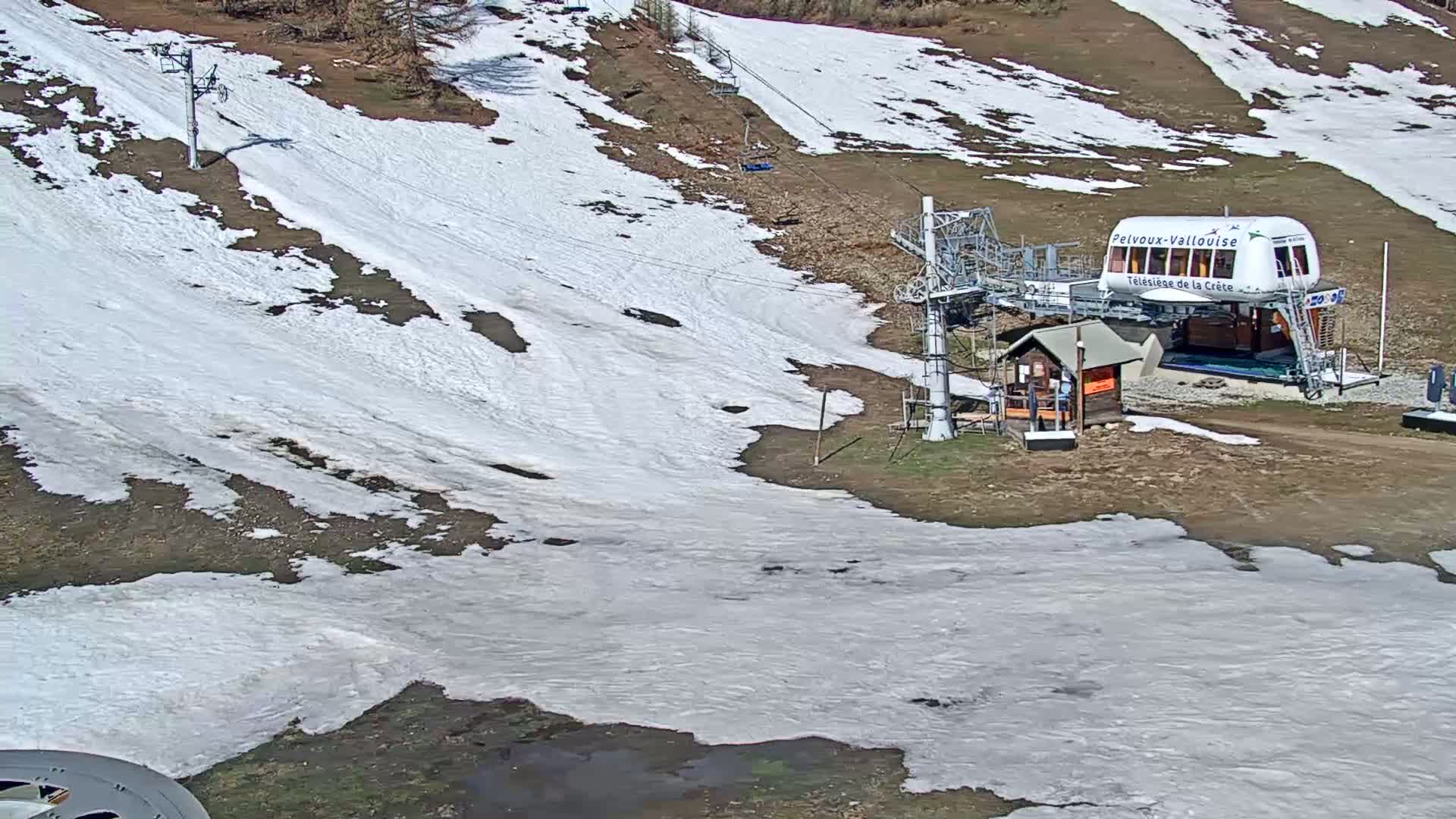 A ski lift and a small building sit on a hillside partially covered in melting snow under a clear sky.