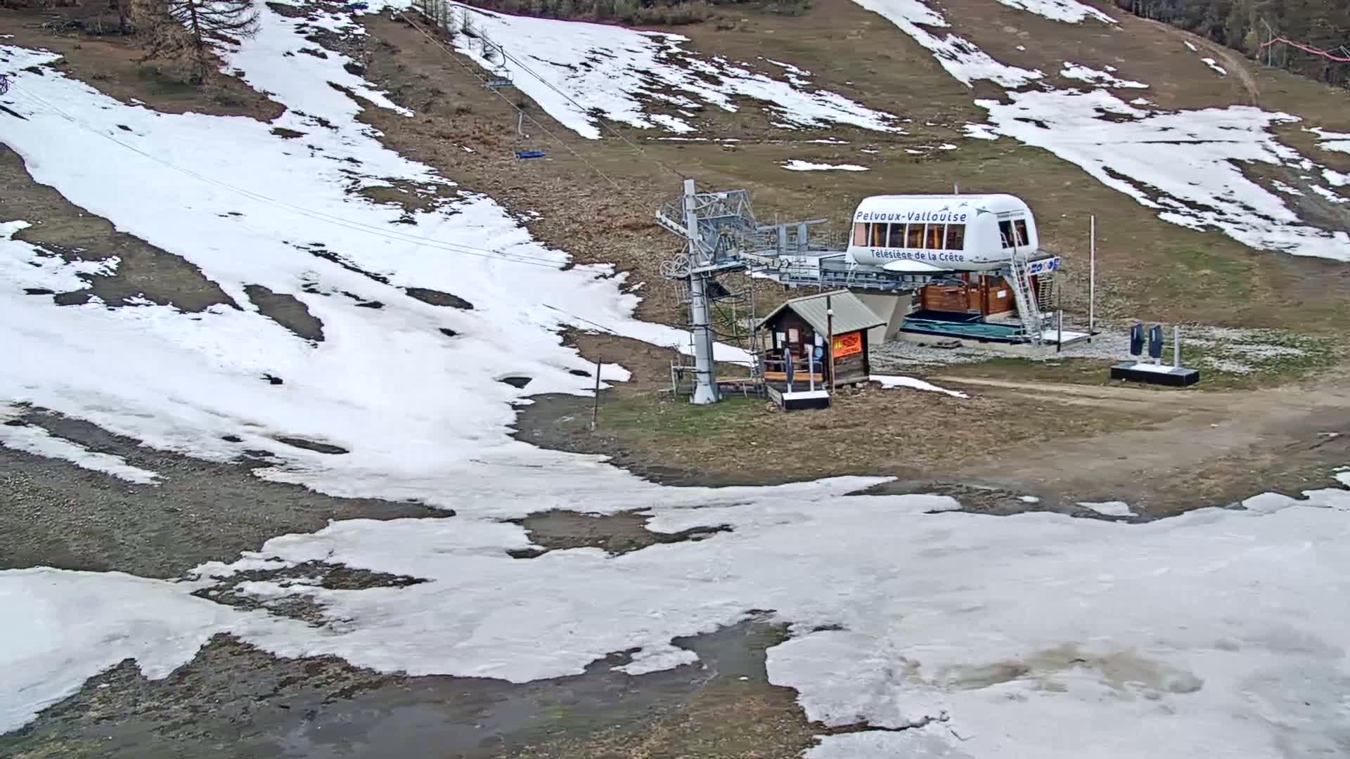 A chairlift station sits on a hillside partially covered in melting snow.