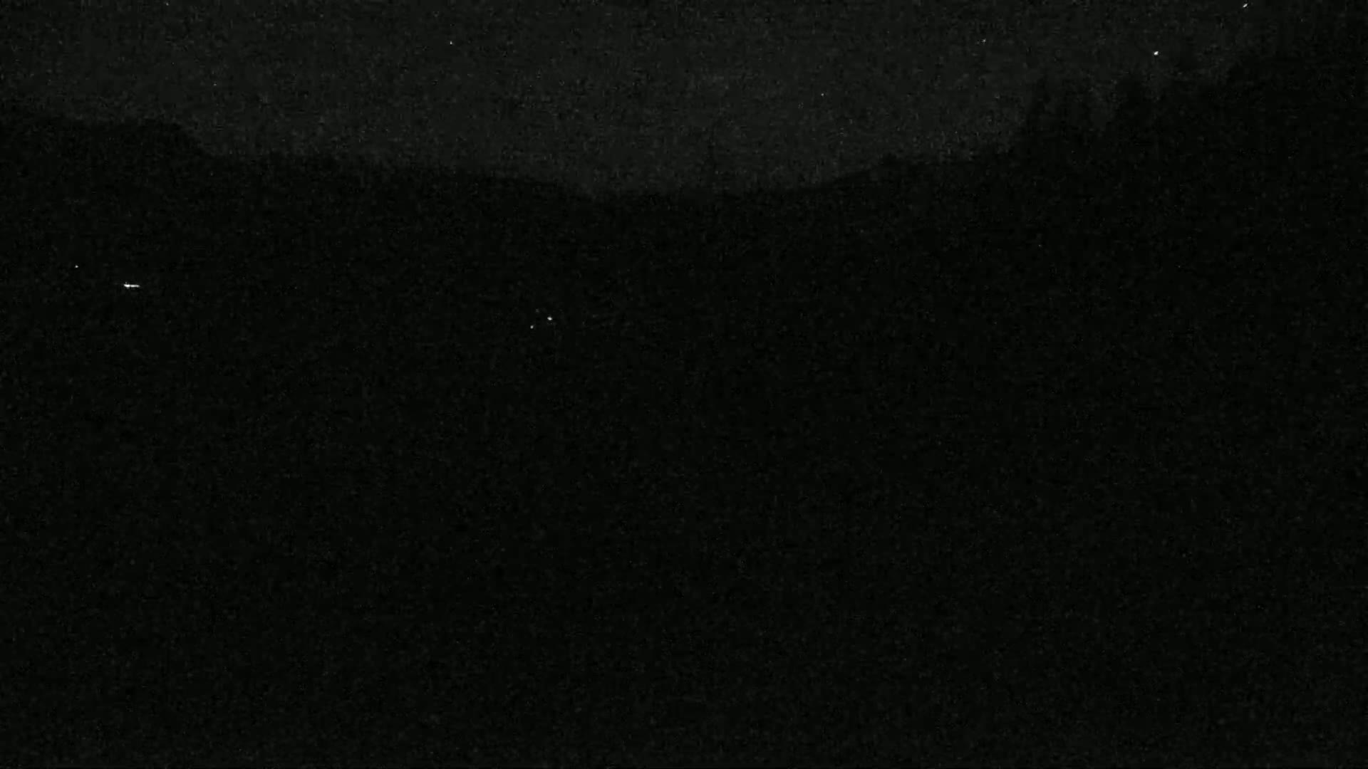 A dark, nighttime landscape is visible with a few faint lights in the distance under a mostly clear sky.