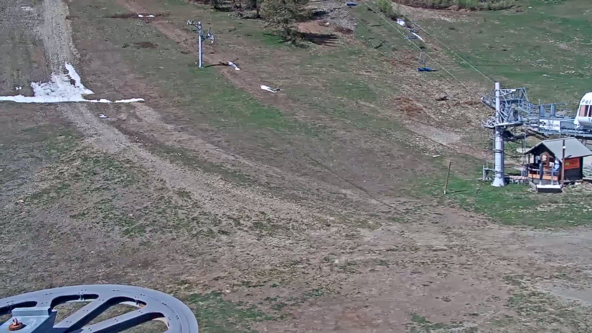 A mostly barren ski slope with patches of grass and small amounts of snow, featuring ski lift equipment.