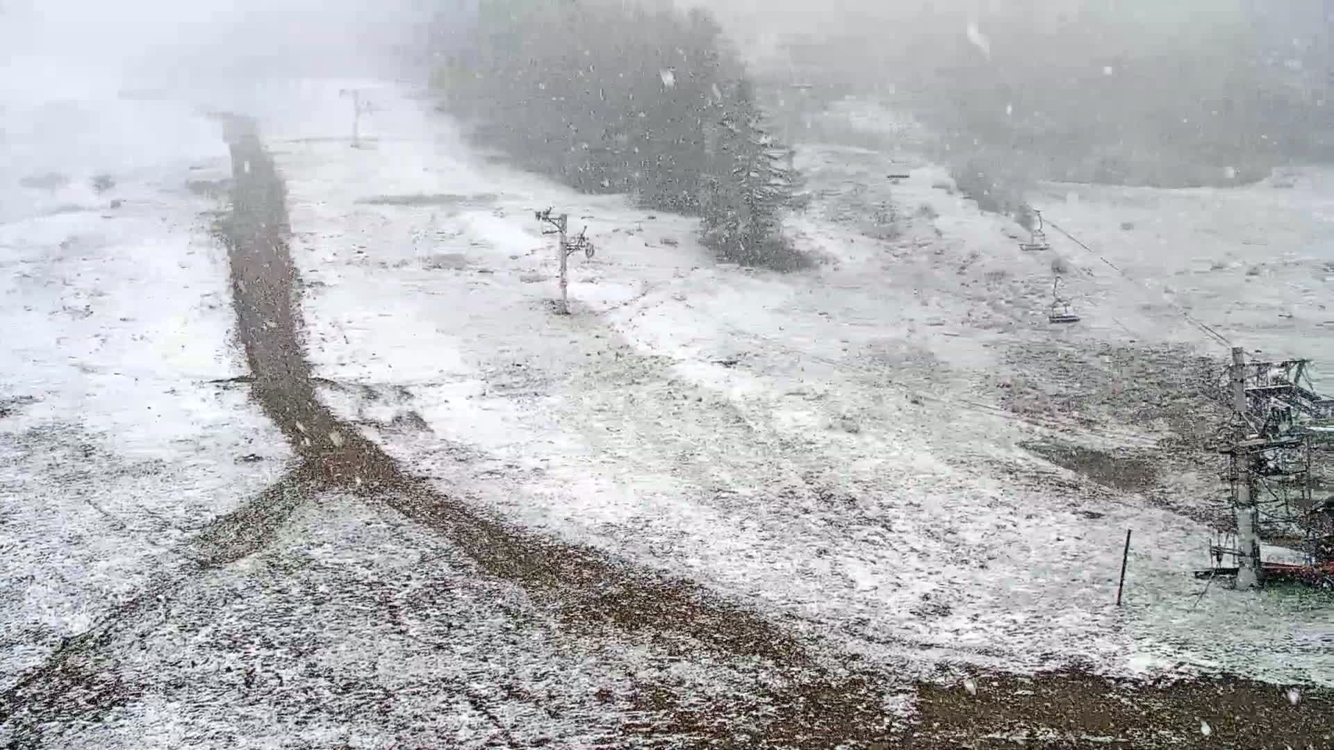 A snow-covered ski slope with several chairlifts is visible during a snowfall.